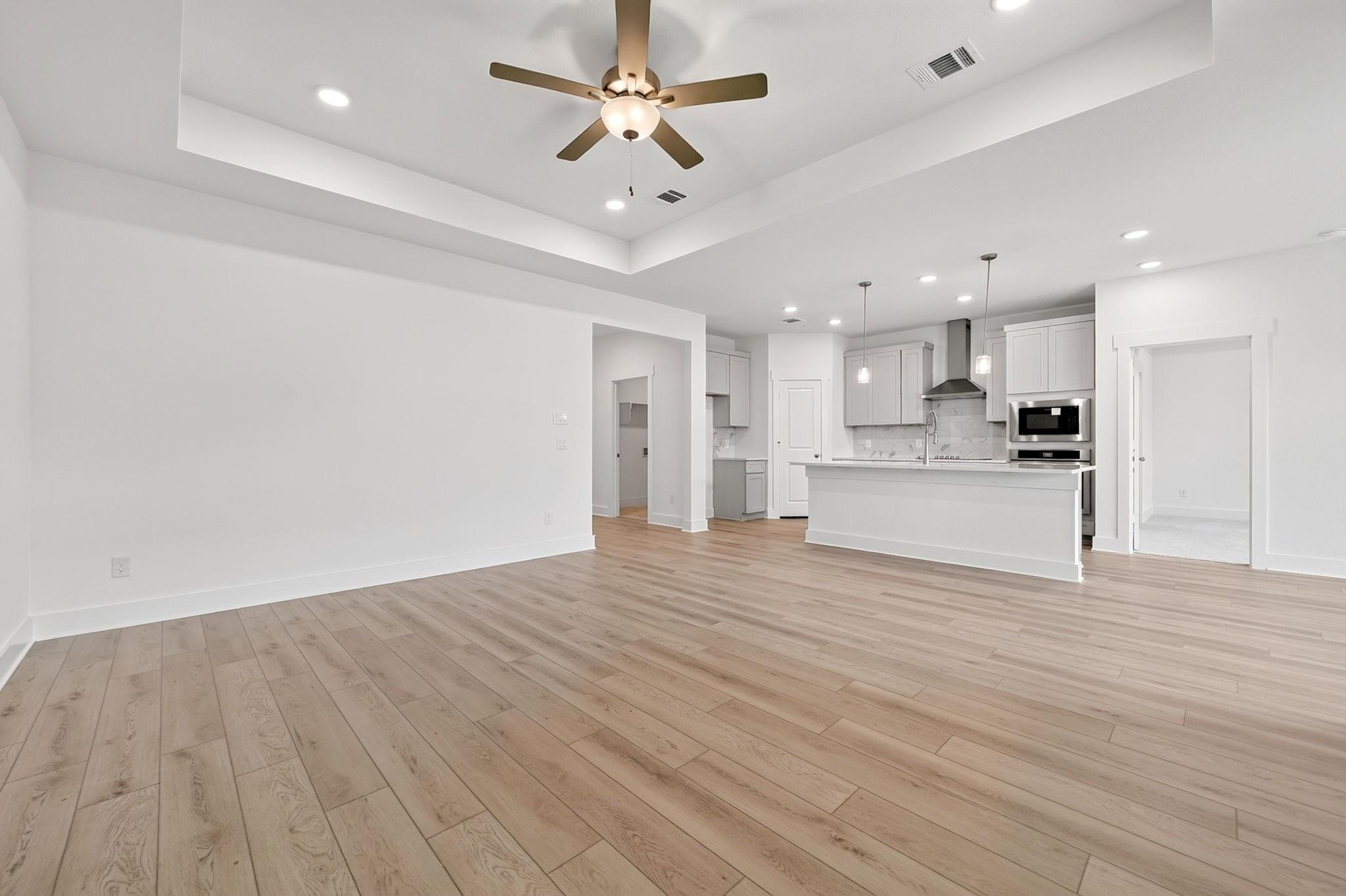 Open-concept living room and kitchen with wood-look flooring and ceiling fan in Davidson Homes The Holly F, Josephine, Texas