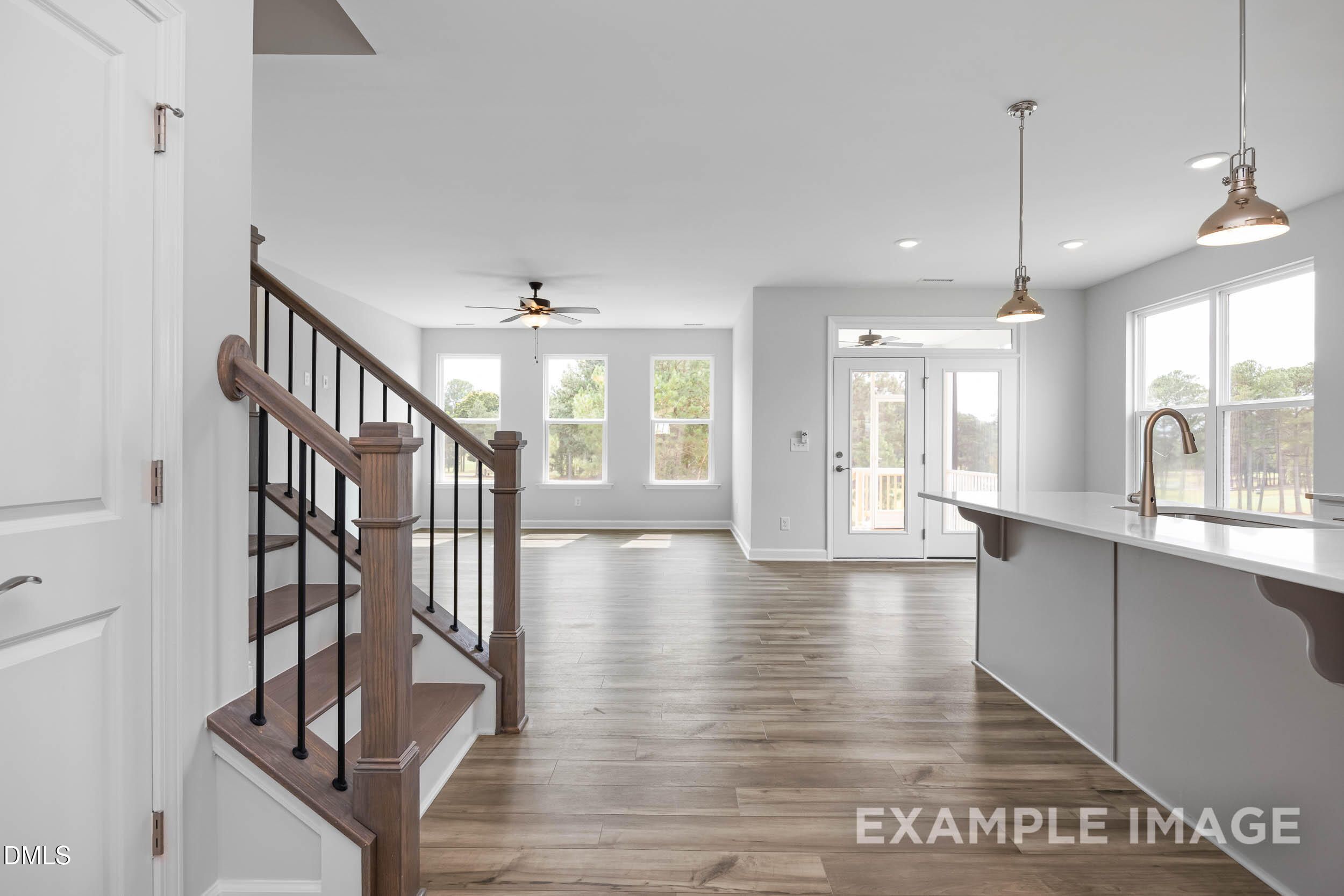 Open foyer with wooden staircase and modern white kitchen island, natural light in The Ash B 3-bedroom home, Lillington, NC