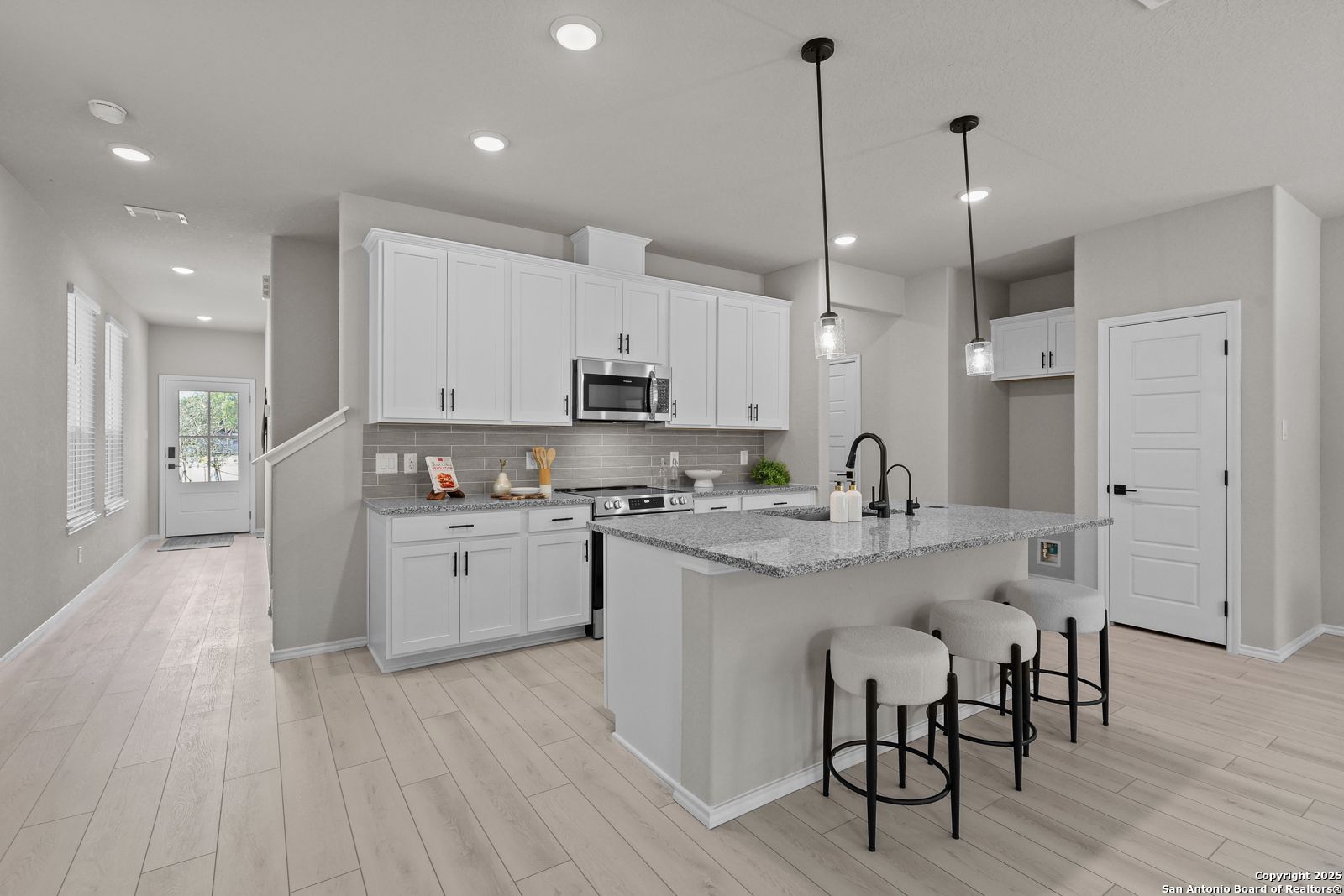 Modern open-concept kitchen with white cabinets, granite island, stainless appliances, and bar stools in Davidson Homes The Charlotte B, San Antonio