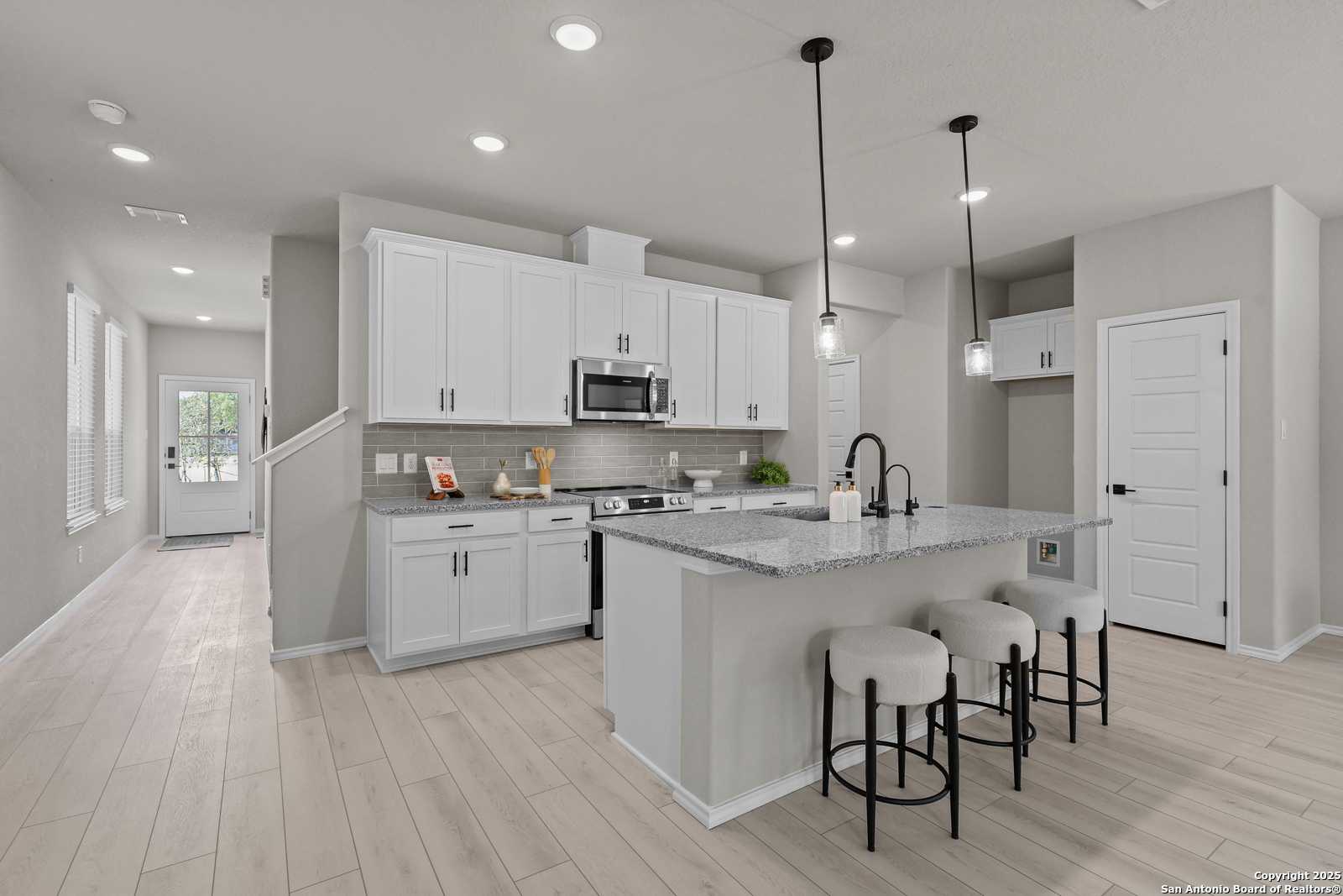 Modern open-concept kitchen with white cabinets, granite island, stainless appliances, and bar stools in Davidson Homes The Charlotte B, San Antonio