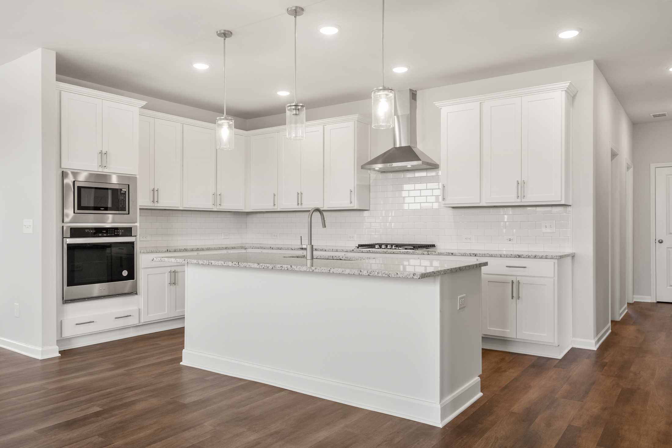Spacious white kitchen at Everleigh in Locust Grove GA with island granite counters stainless steel appliances subway tile and hardwood floors