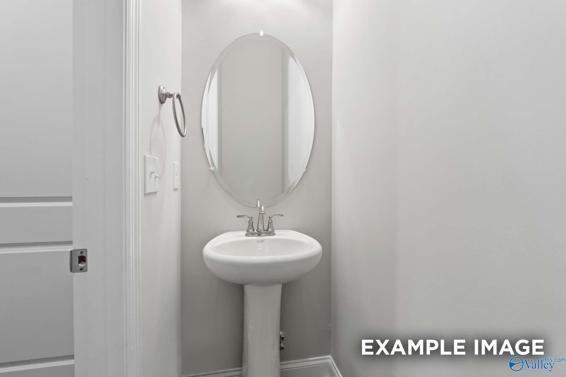 Elegant powder room featuring white pedestal sink and oval mirror in Evermore Homes The Haven E, Owens Cross Roads, Alabama