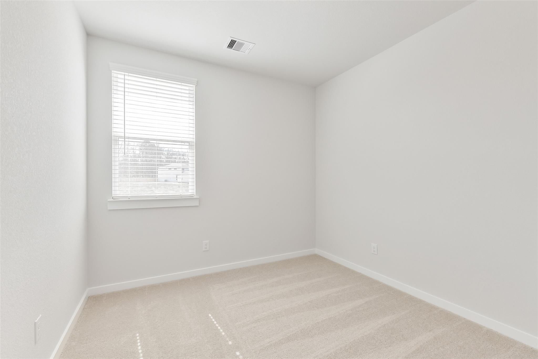 Bright empty secondary bedroom with white walls, beige carpet, and window blinds in Davidson Homes The Colorado F, Cleveland, Texas