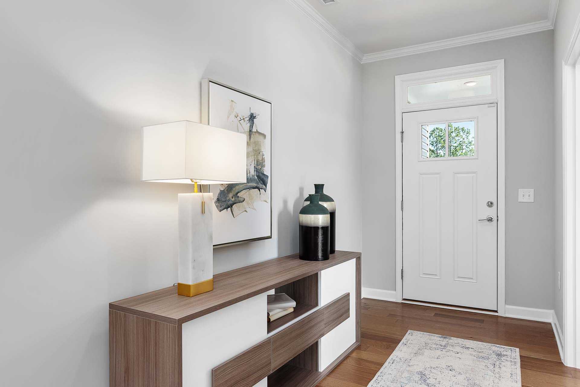 Elegant entryway at Highland Forest in Fuquay-Varina NC with gray walls, console table, marble lamp, abstract art, and white door