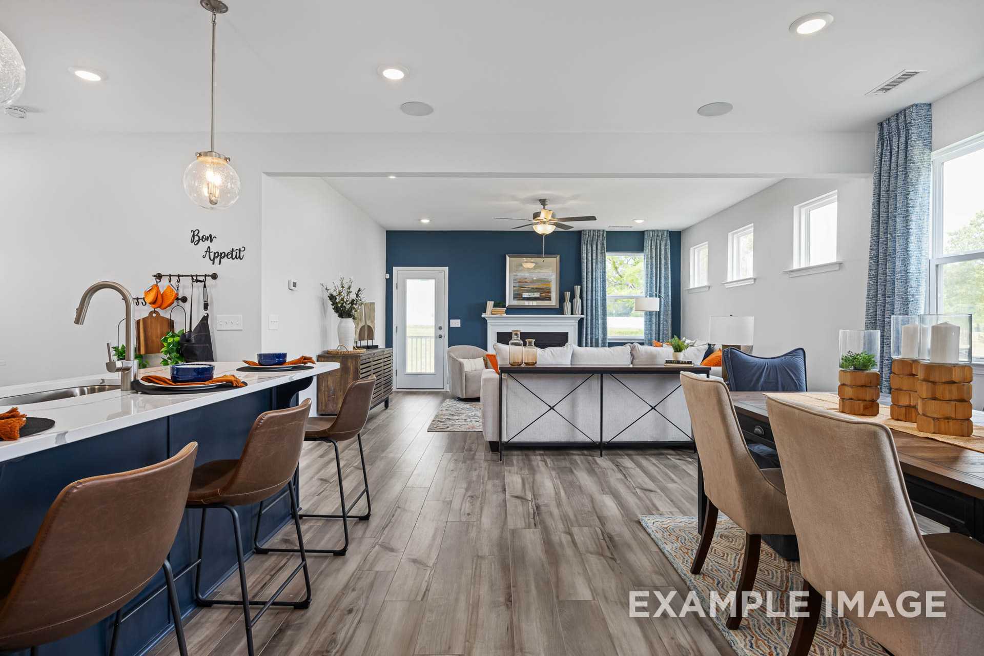 Open-concept kitchen and living room in The Adalynn A with blue island, fireplace, pendant lights, and hardwood floors