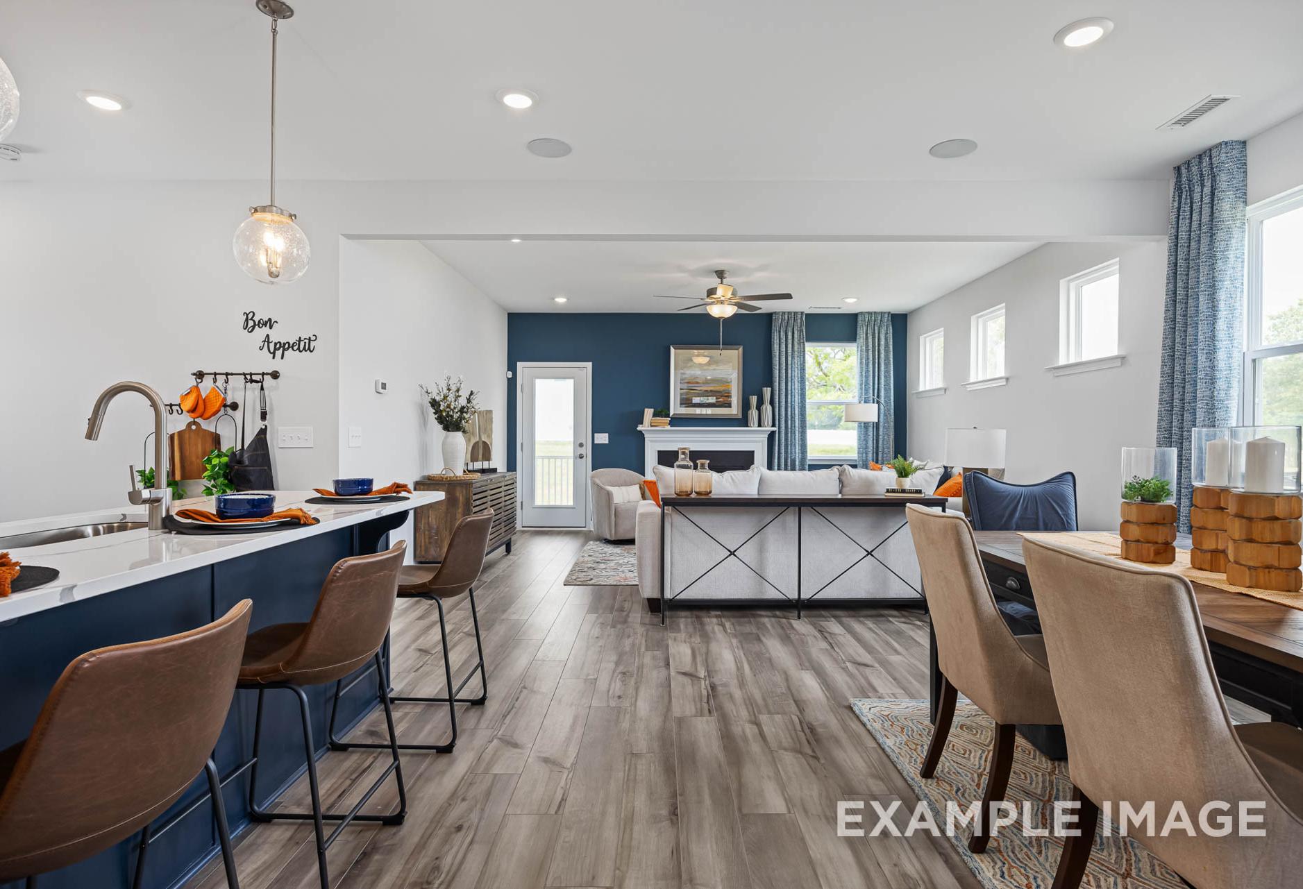 Open-concept kitchen and living room in The Adalynn A with blue island, fireplace, pendant lights, and hardwood floors