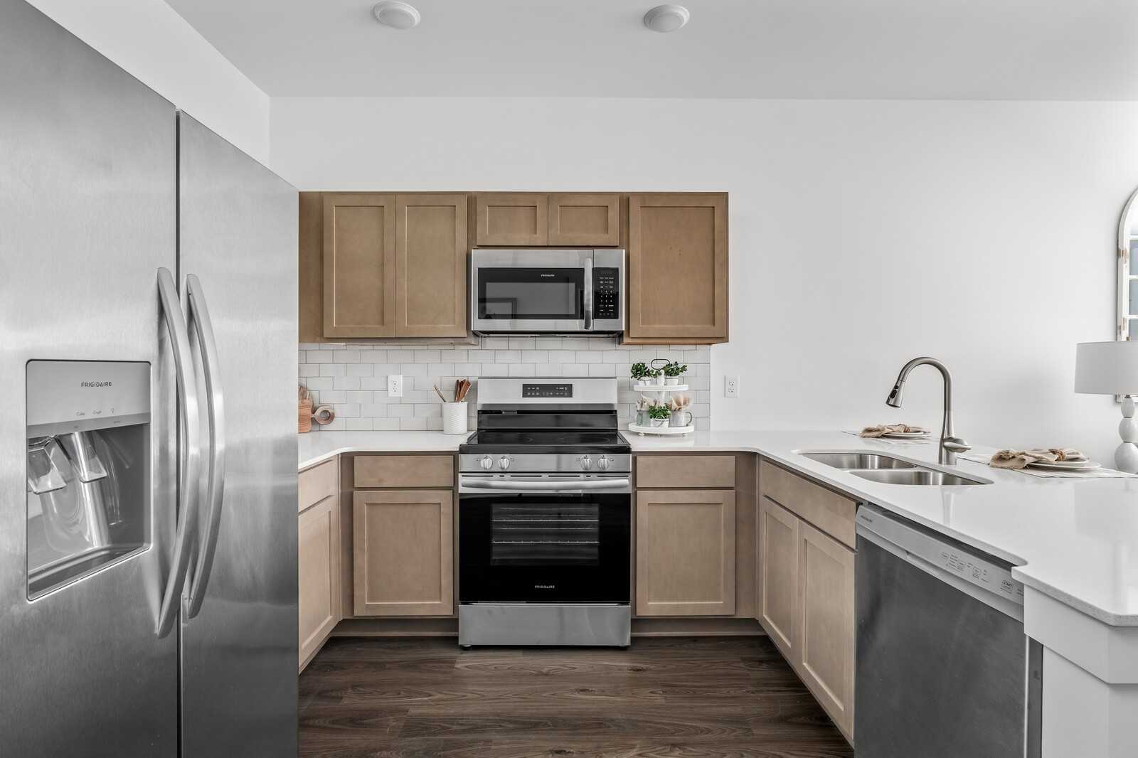 Open-concept kitchen with stainless steel appliances, white quartz counters, and beige shaker cabinets in Davidson Homes Cumberland A, Gallatin, TN