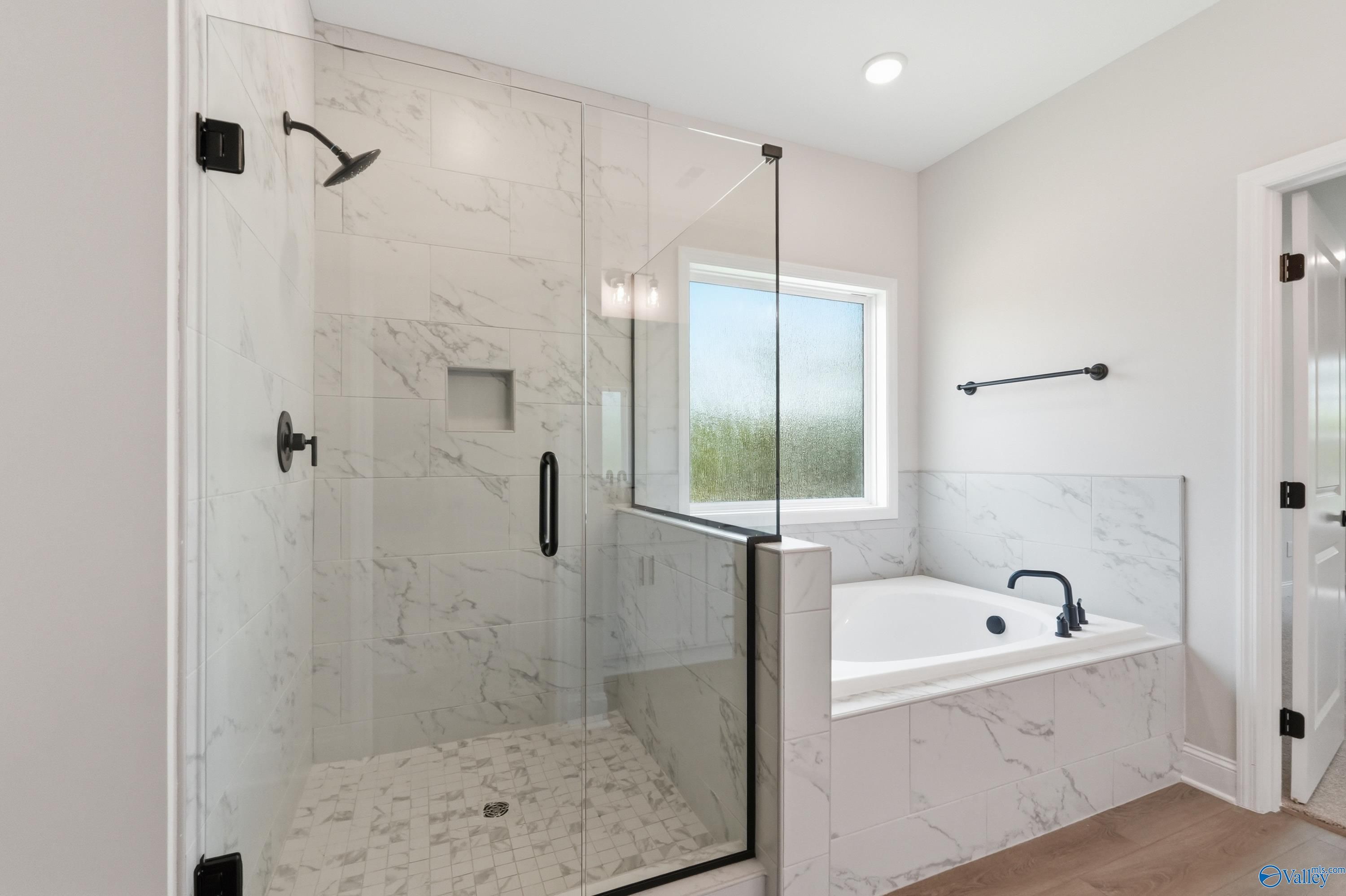 Elegant master bathroom with frameless glass shower, marble tiles, soaking tub, and garden window in Davidson Homes The Rockford B, Athens AL