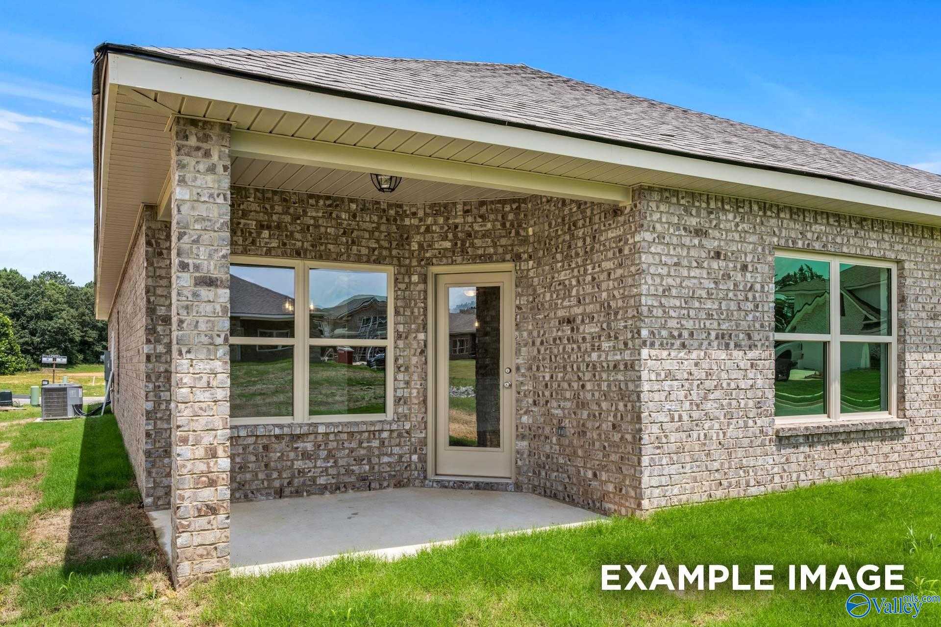 Beige brick single-story home with large windows, covered entry porch, and lush green lawn in The Highlands, Arab, Alabama