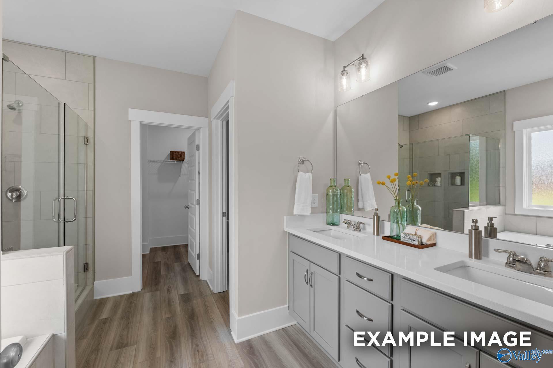 Primary bathroom with dual vanity, walk-in tile shower, and wood-look floors in Davidson Homes Everett B, Arab, Alabama