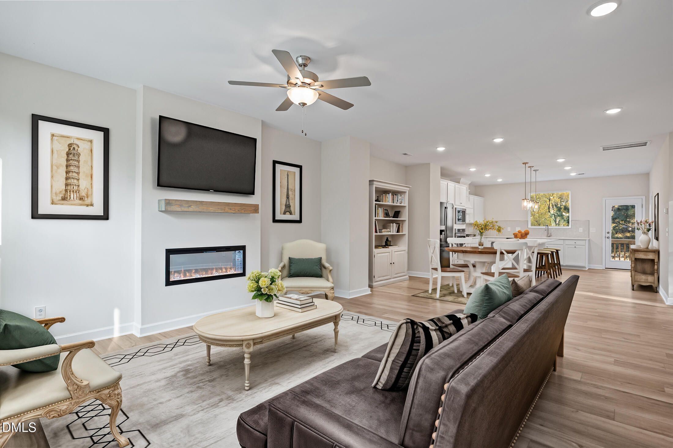 Spacious open living room with linear gas fireplace, mounted TV, Eiffel Tower art, plush sofa, and adjacent kitchen in Davidson Homes The Avery, Knightdale NC