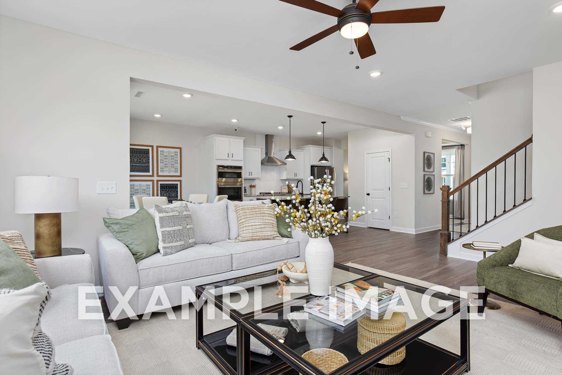 Spacious open-concept living room in The Willow F with gray sectional sofa, ceiling fan, and adjacent white kitchen island