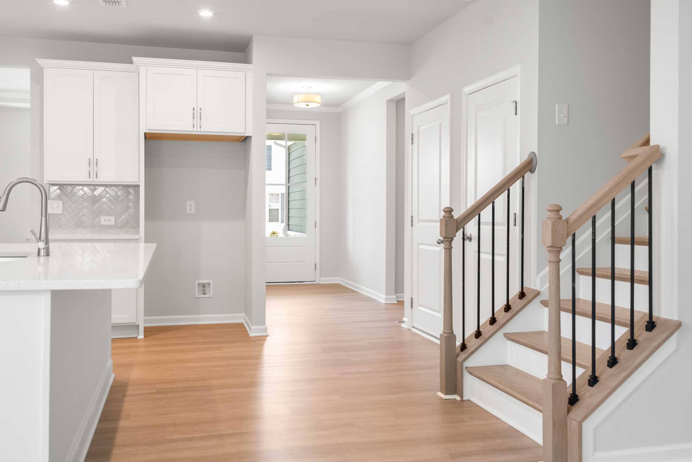 Open-concept kitchen with white cabinets, quartz island, hardwood floors, and oak staircase in The Ash B by Davidson Homes, Hoschton GA