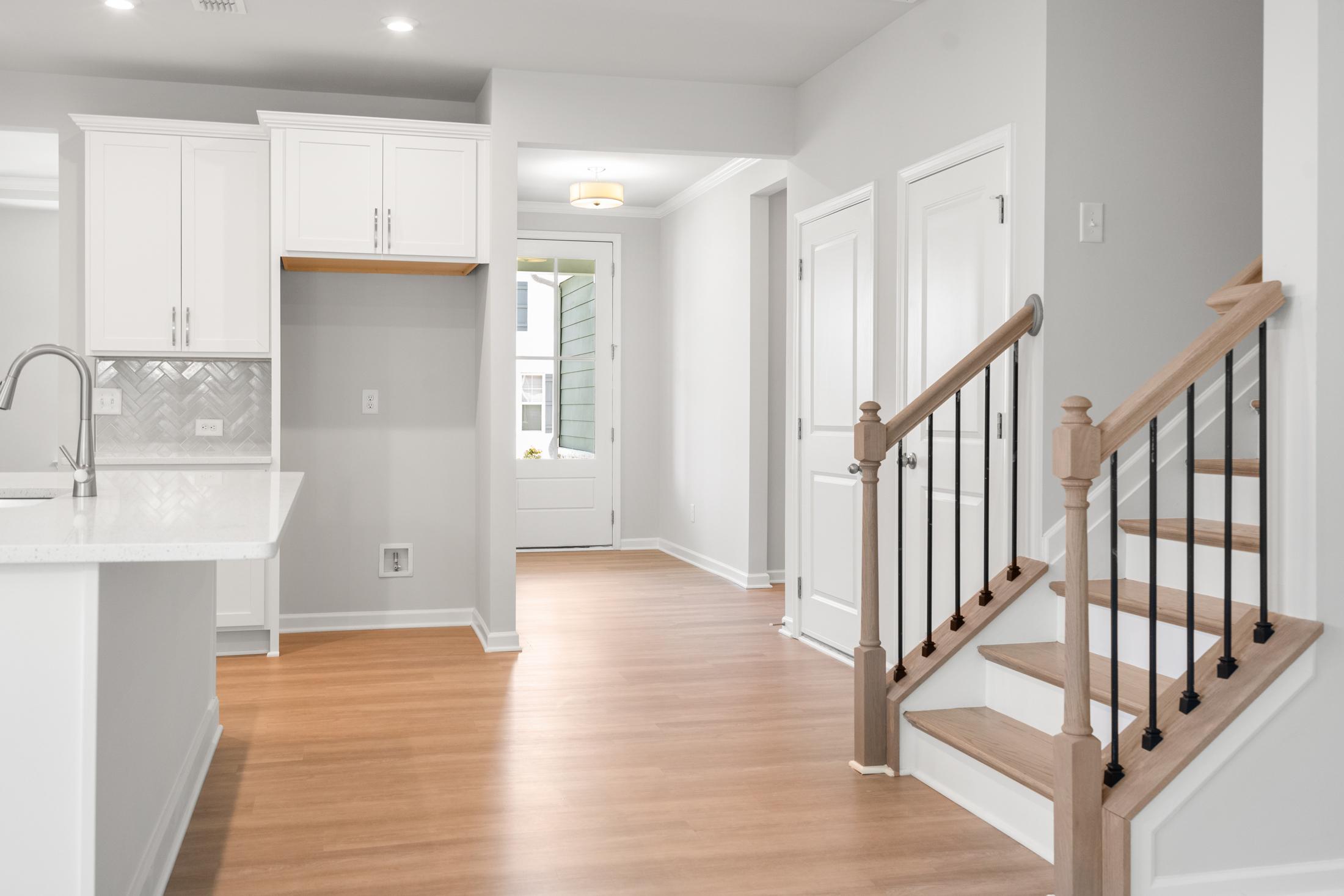 Open-concept kitchen with white cabinets, quartz island, hardwood floors, and oak staircase in The Ash B by Davidson Homes, Hoschton GA