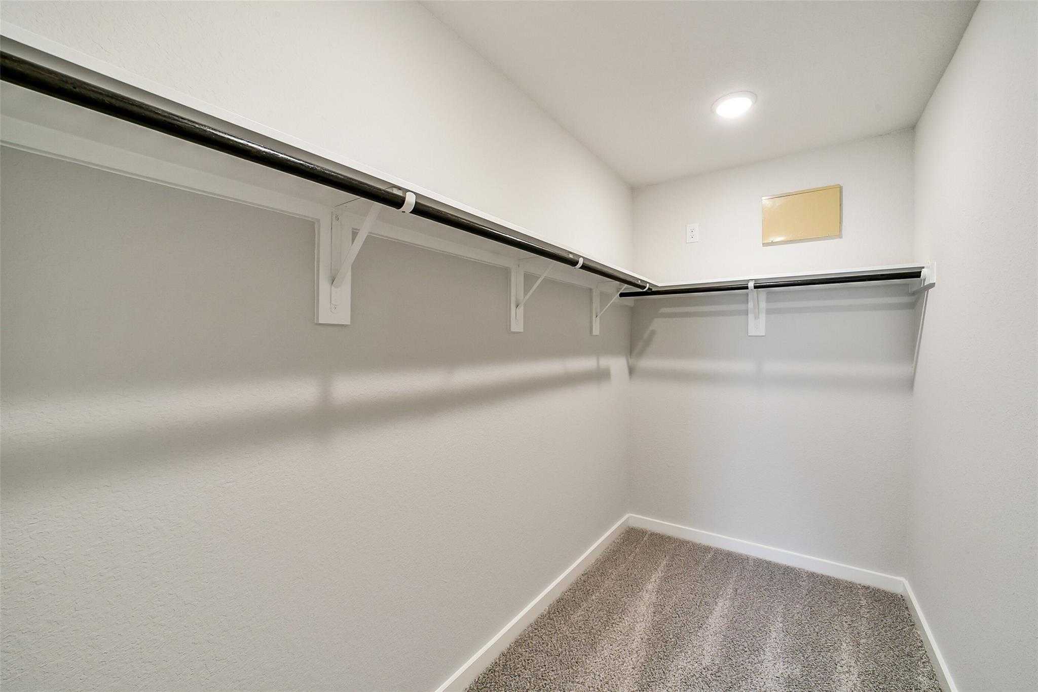 Spacious walk-in closet with black metal hanging rods, white brackets, and carpeted floor in Davidson Homes The Trinity F, Magnolia, Texas