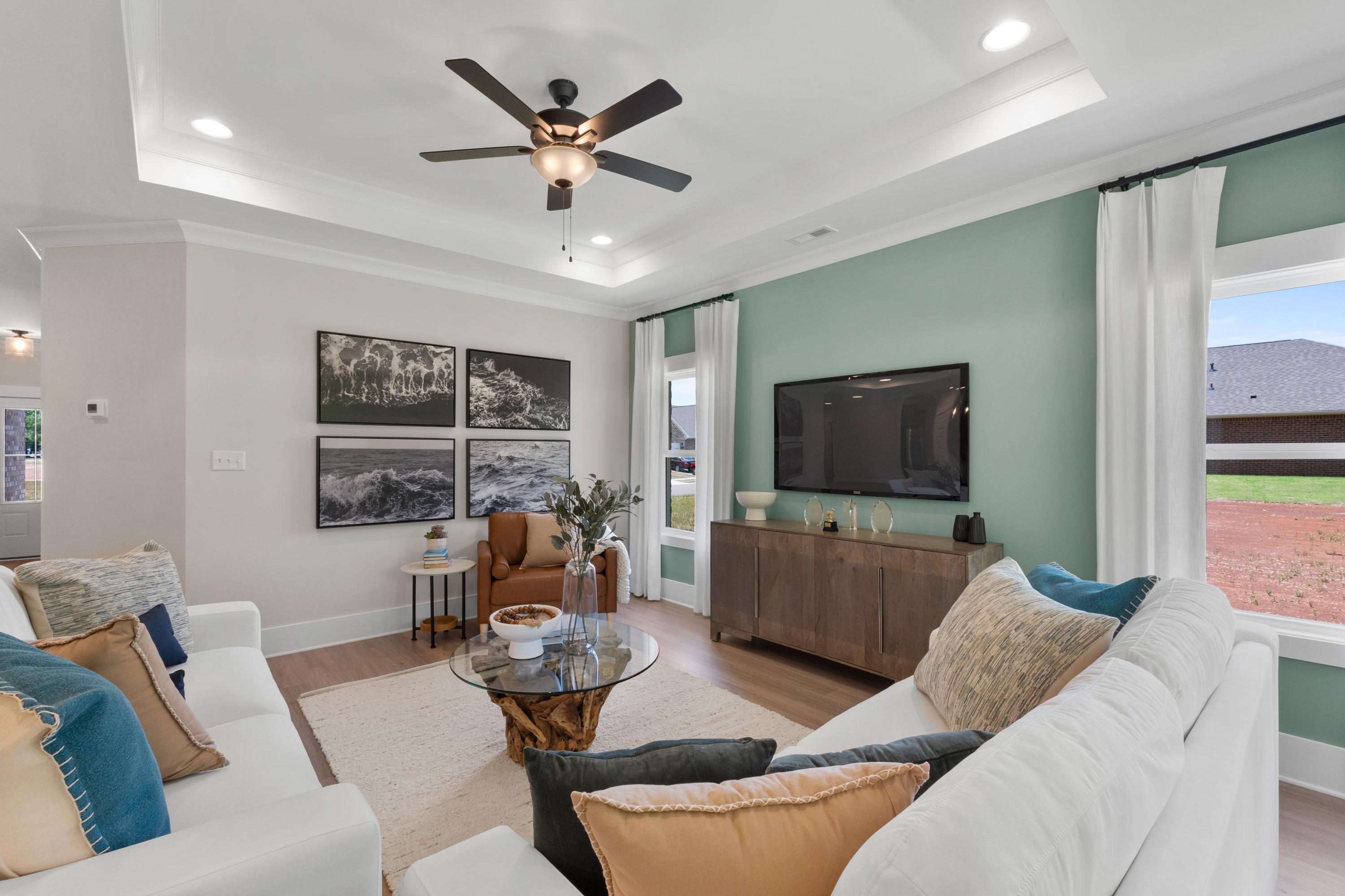 Spacious living room at Hollon Meadow in Decatur Alabama with white sofa, hardwood floors, ceiling fans, and large windows to green yard