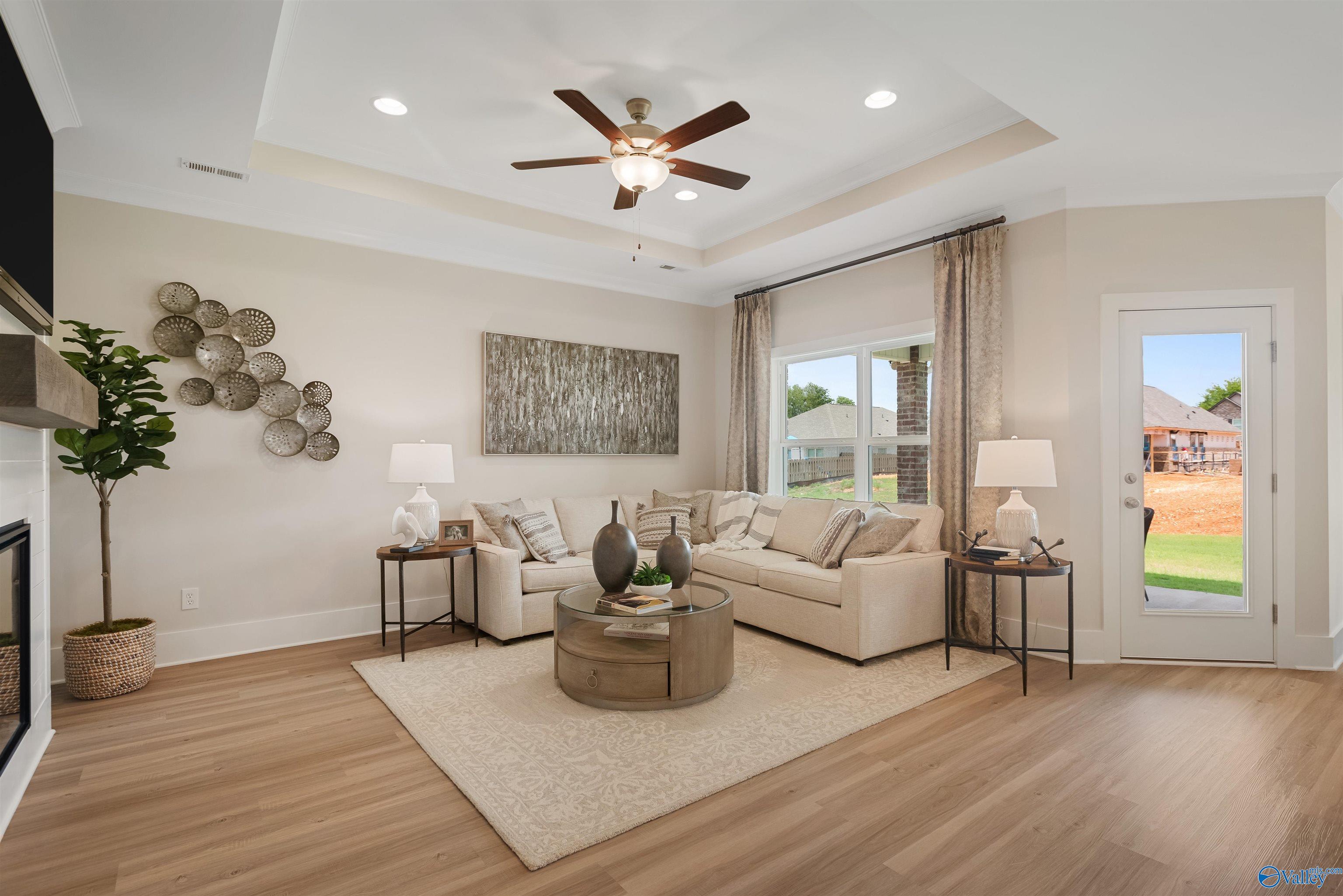 Cozy beige living room with sectional sofa, fireplace, potted plants, and yard-view windows in Davidson Homes The Everett, New Market, Alabama