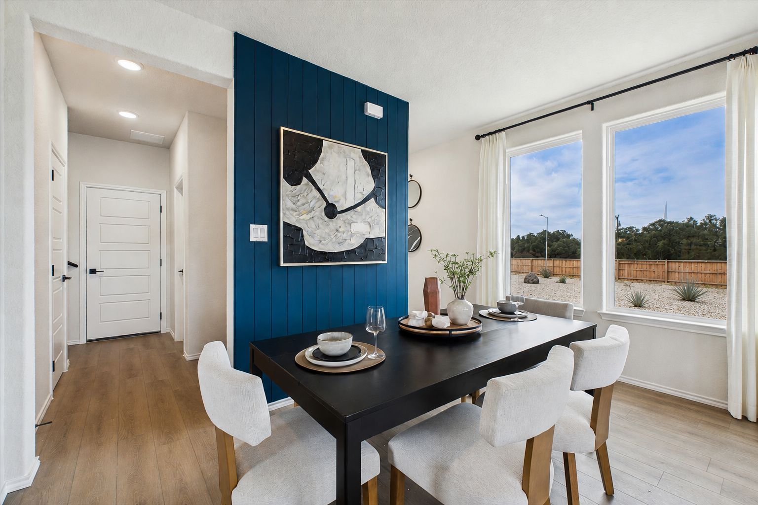 Spacious dining room in Meadows at Oak Creek San Antonio TX with navy blue accent wall, abstract art, black table, white chairs, hardwood floors