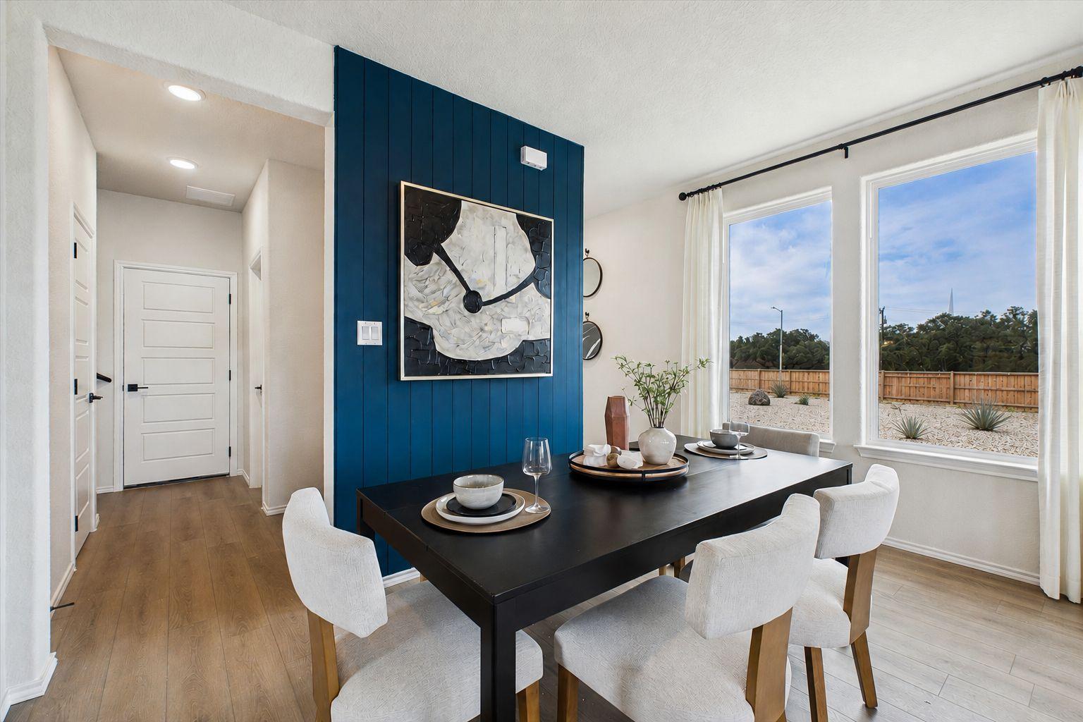 Spacious dining room in Meadows at Oak Creek San Antonio TX with navy blue accent wall, abstract art, black table, white chairs, hardwood floors