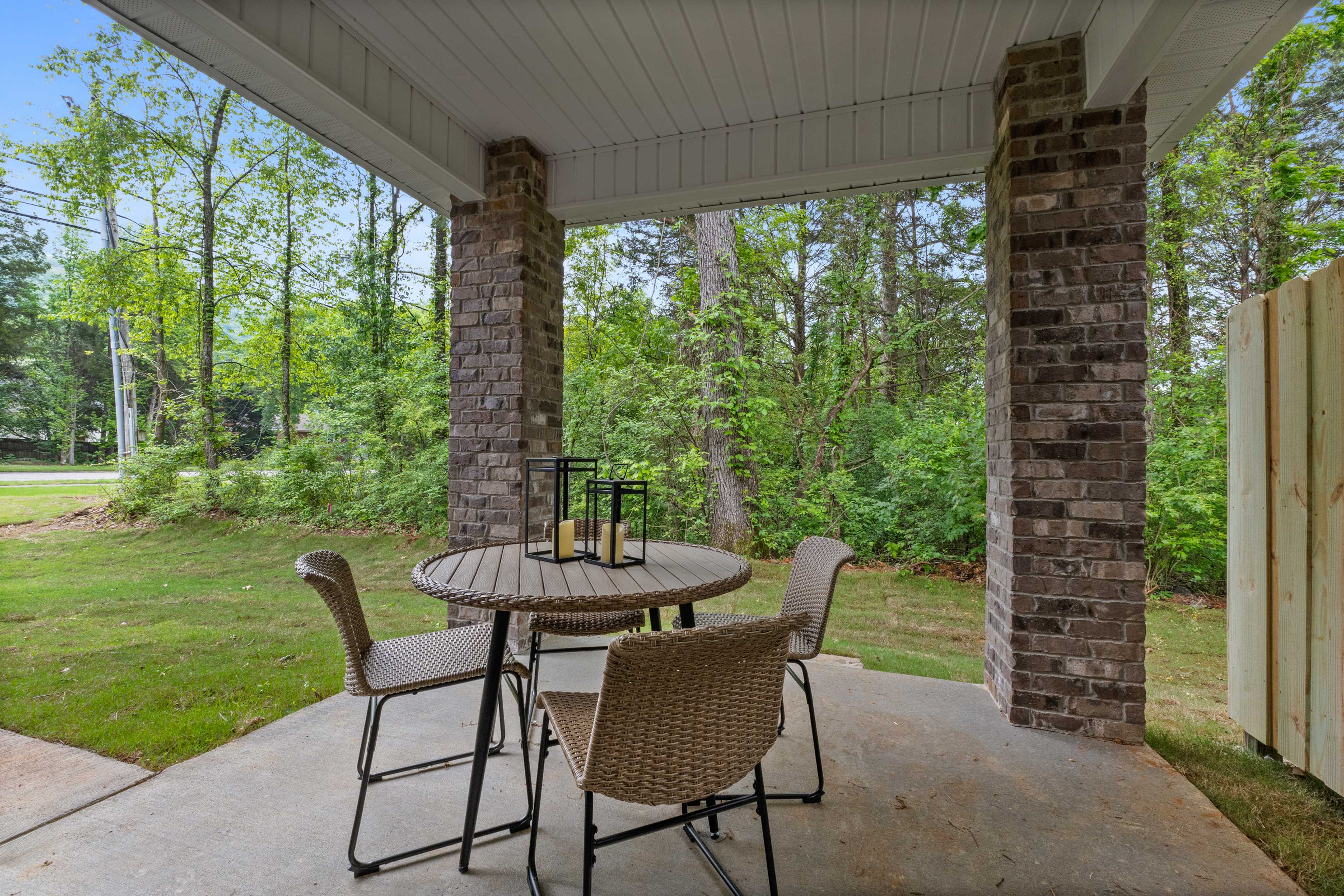 Covered patio with round wicker dining set and lanterns at Pavilion in Huntsville Alabama surrounded by brick pillars and lush trees