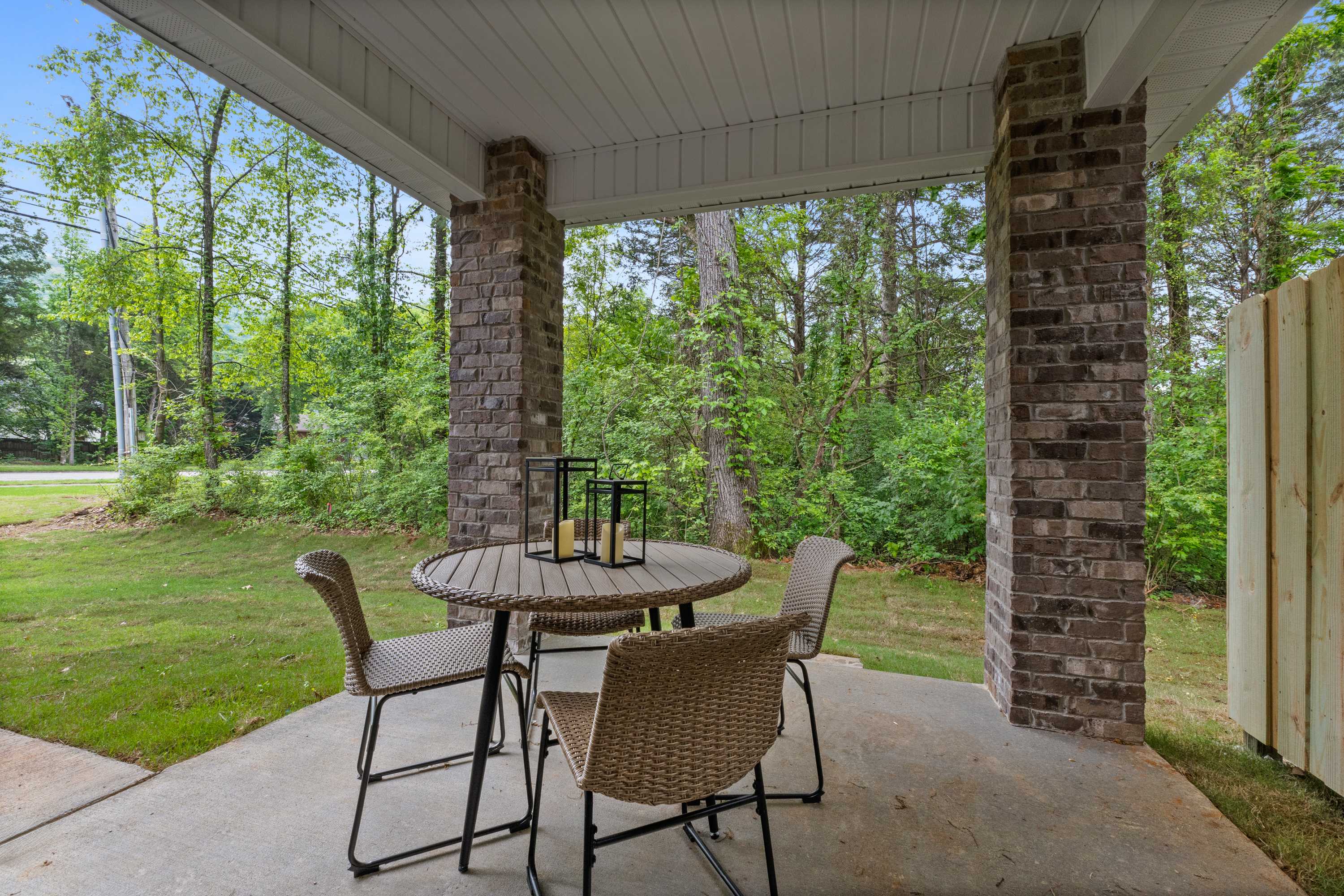Covered patio with round wicker dining set and lanterns at Pavilion in Huntsville Alabama surrounded by brick pillars and lush trees