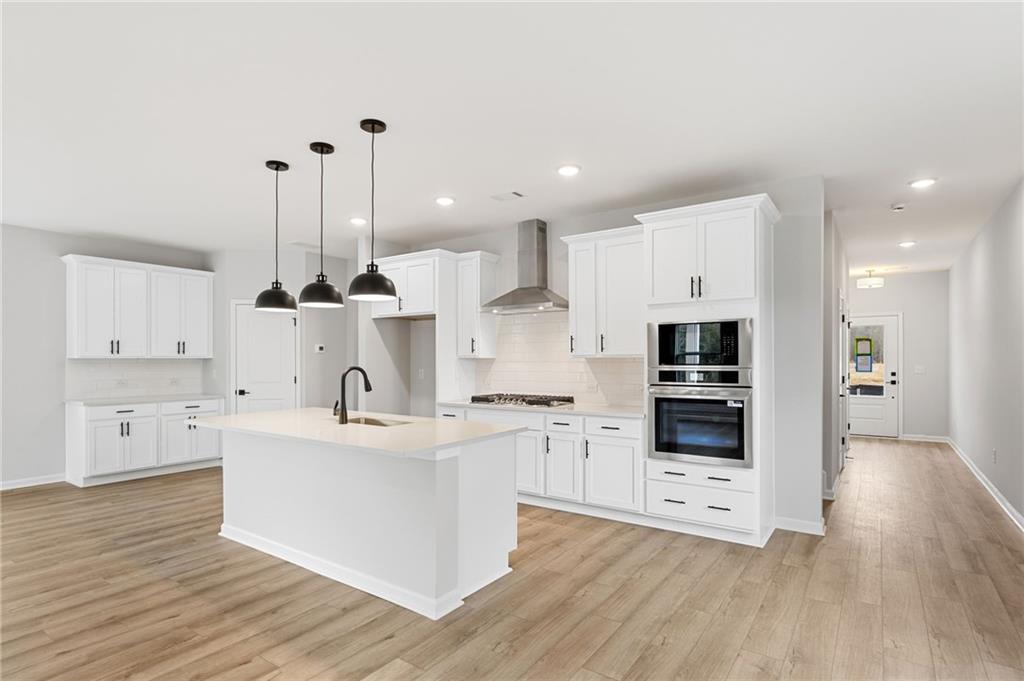 Modern white kitchen featuring large island, stainless double oven, pendant lights in Davidson Homes The Rabun C, Winder, GA