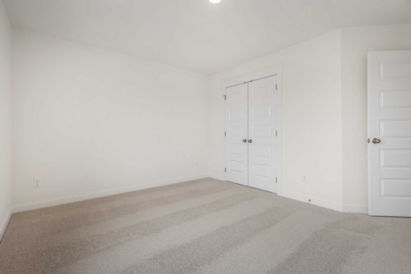 Bright secondary bedroom with white walls, beige carpet, and double closet doors in Davidson Homes The Logan C, Gallatin, TN