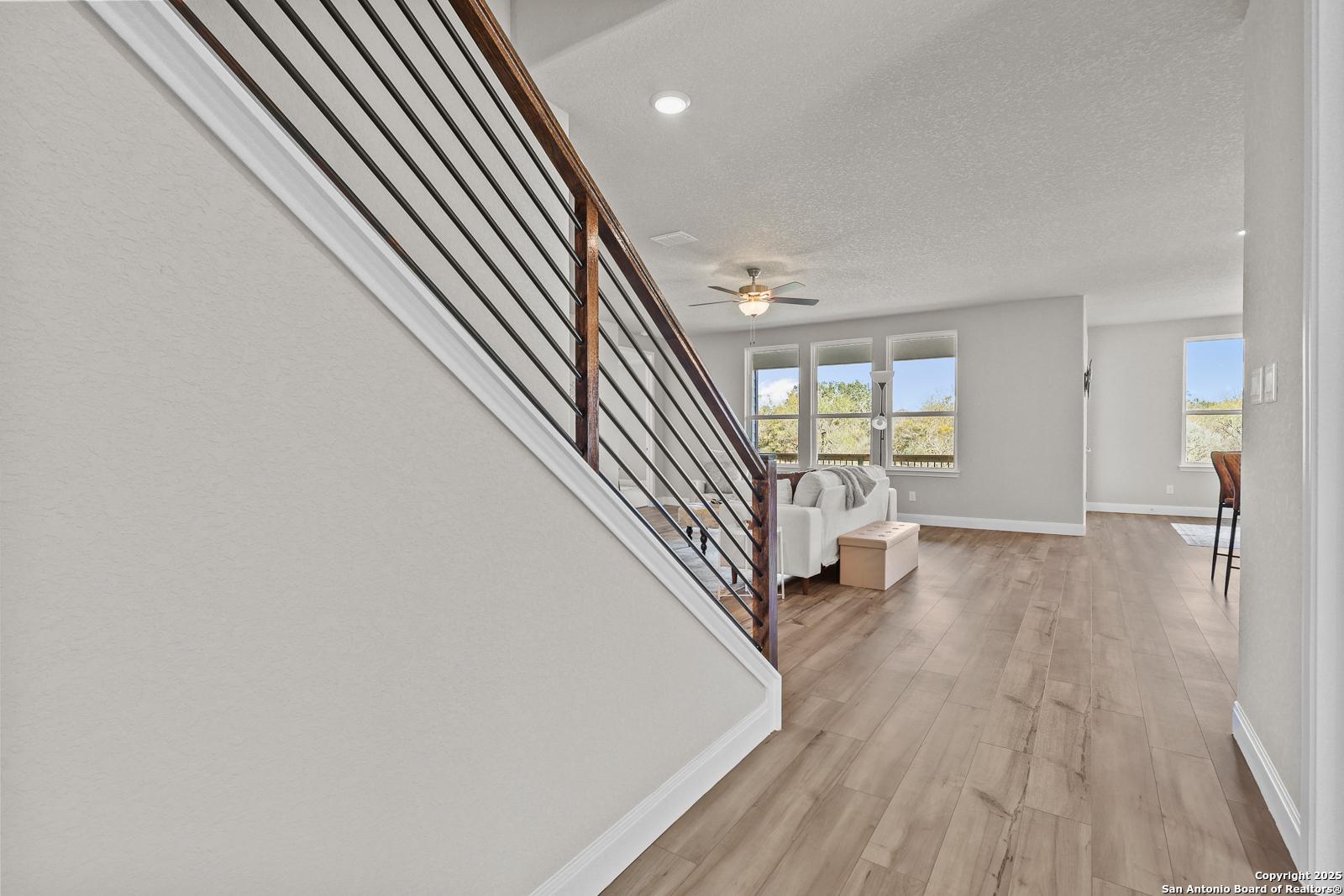 Elegant two-story staircase with dark metal railing and hardwood floors in open living room of Davidson Homes The Jennings G, Castroville, Texas