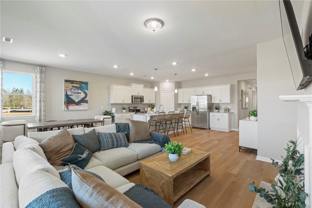Open-concept living room with white L-shaped sofa, fireplace, and kitchen island in Davidson Homes The Phoenix B, Opelika, Alabama