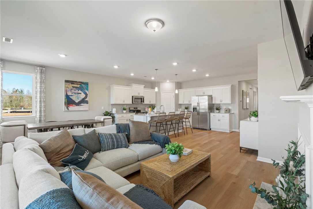 Open-concept living room with white L-shaped sofa, fireplace, and kitchen island in Davidson Homes The Phoenix B, Opelika, Alabama