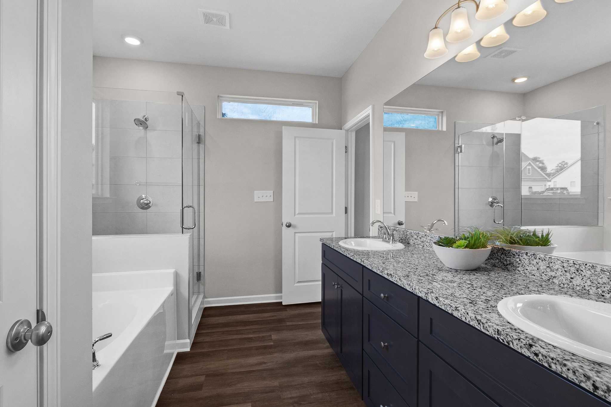 Spacious primary bathroom at Ivy Glen in Perry Georgia with navy double vanity, granite counters, walk-in shower, and soaking tub