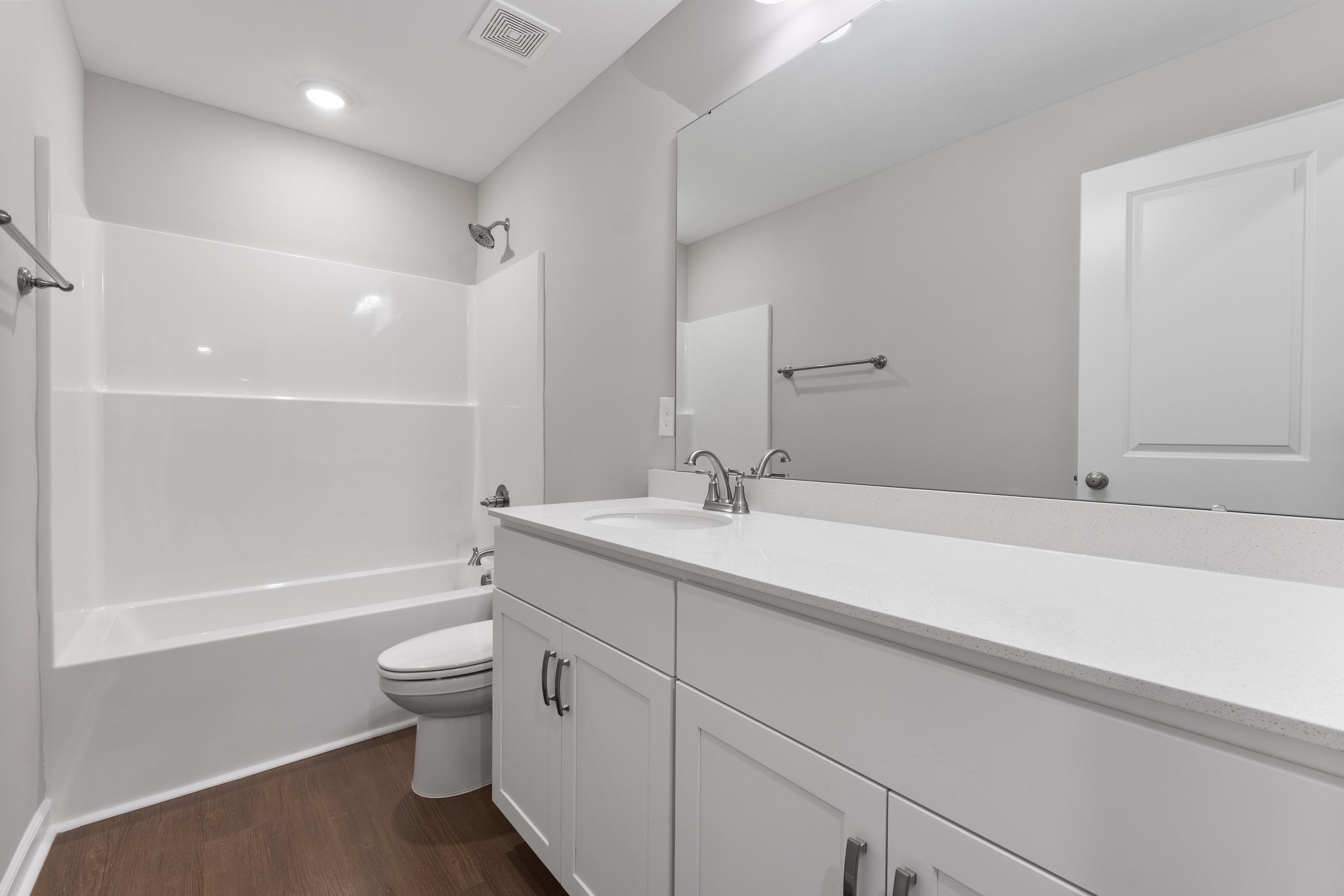 Spacious master bathroom in The Avalon D with white tub-shower combo, modern vanity, toilet, gray walls, and hardwood floors