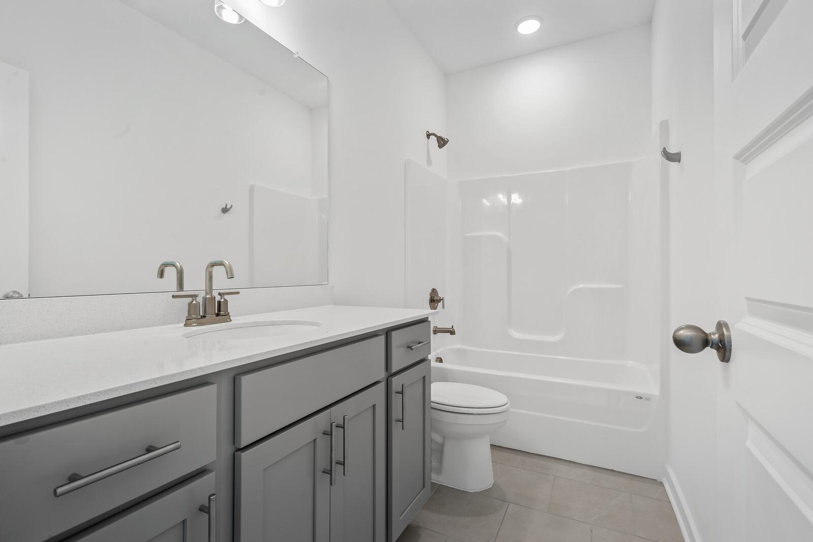 Bright guest bathroom in The Asheville home with gray vanity, white tub, modern faucet, and tiled floor