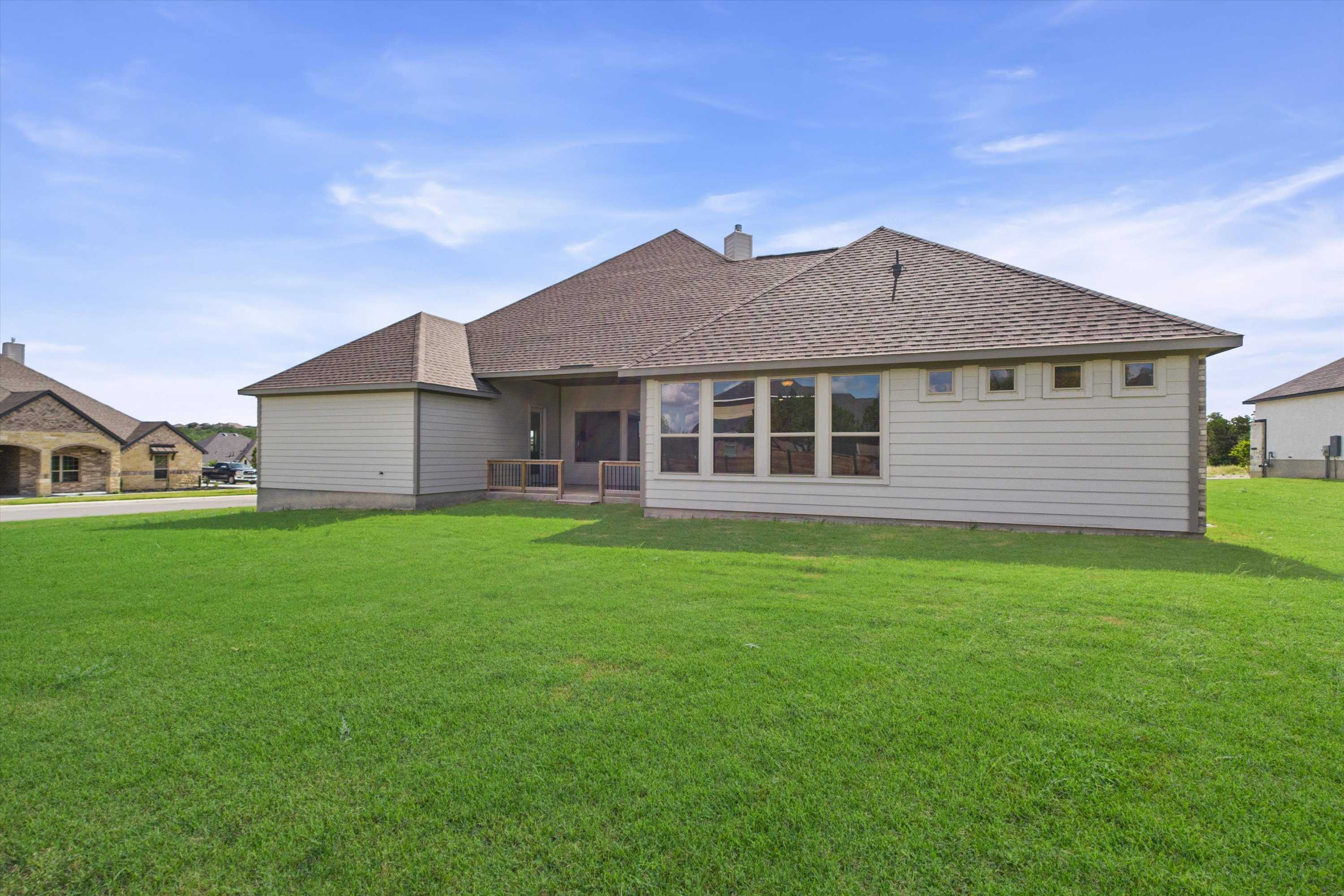 Rear view of The Summerlin C single-story home featuring covered patio, large windows, and lush green yard in Potranco Oaks, Castroville, Texas