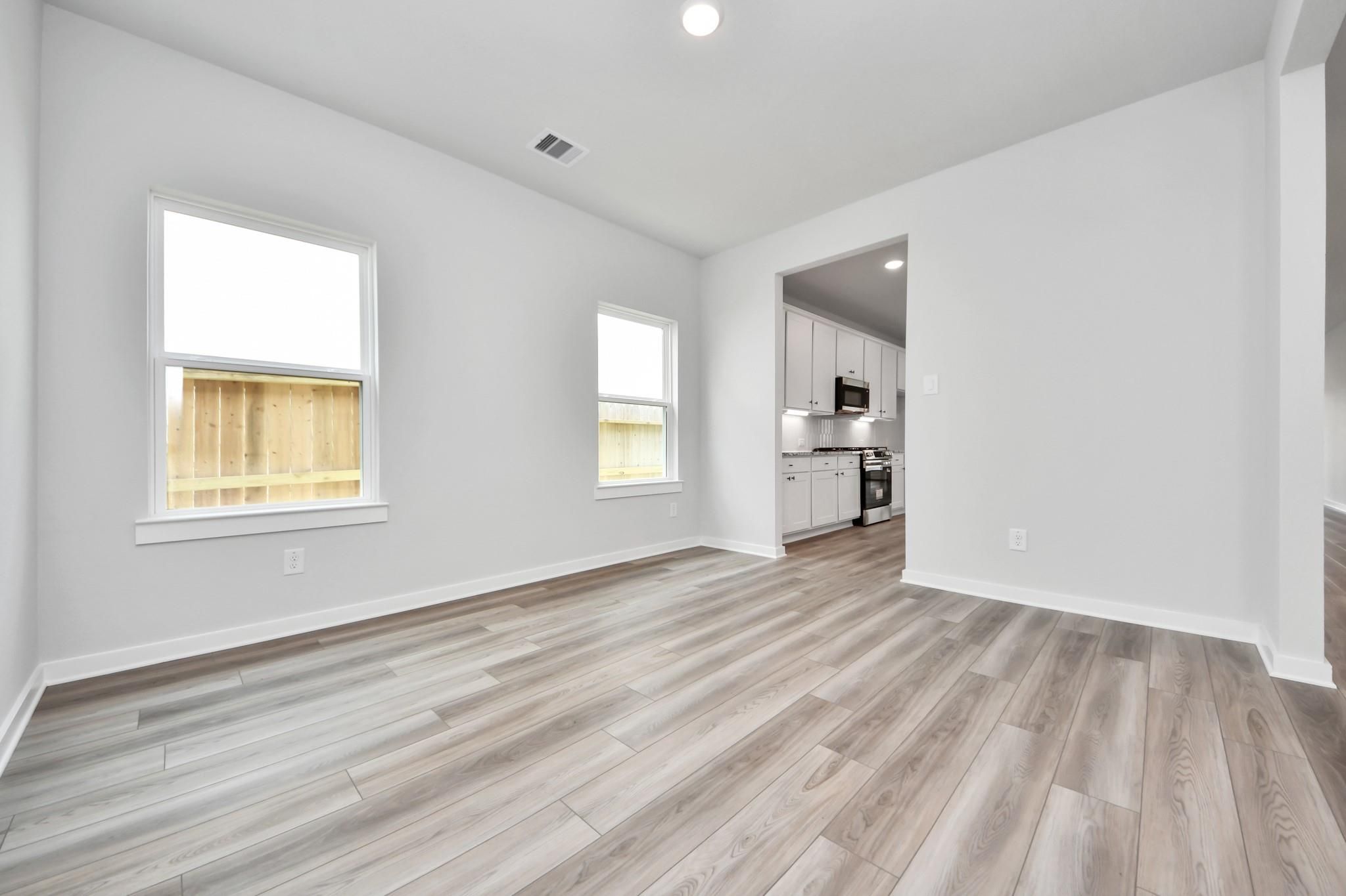 Bright dining area with wood-look flooring opening to a modern kitchen in a Davidson Homes Sorrento E plan, Crosby, Texas.