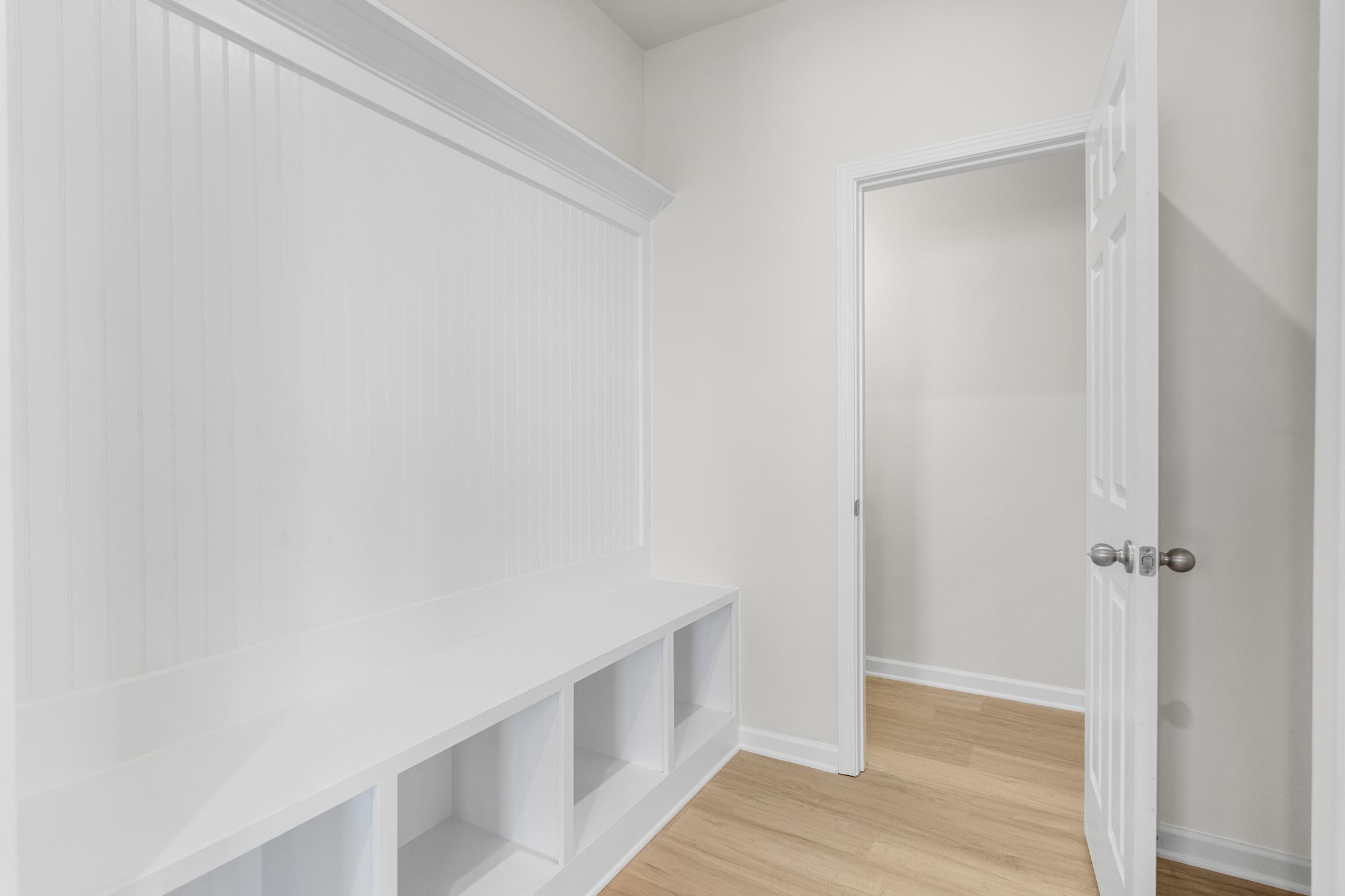 Spacious mudroom in The Glenwood A with white wainscoting, built-in benches, cubbies, and oak flooring in Hoschton GA home
