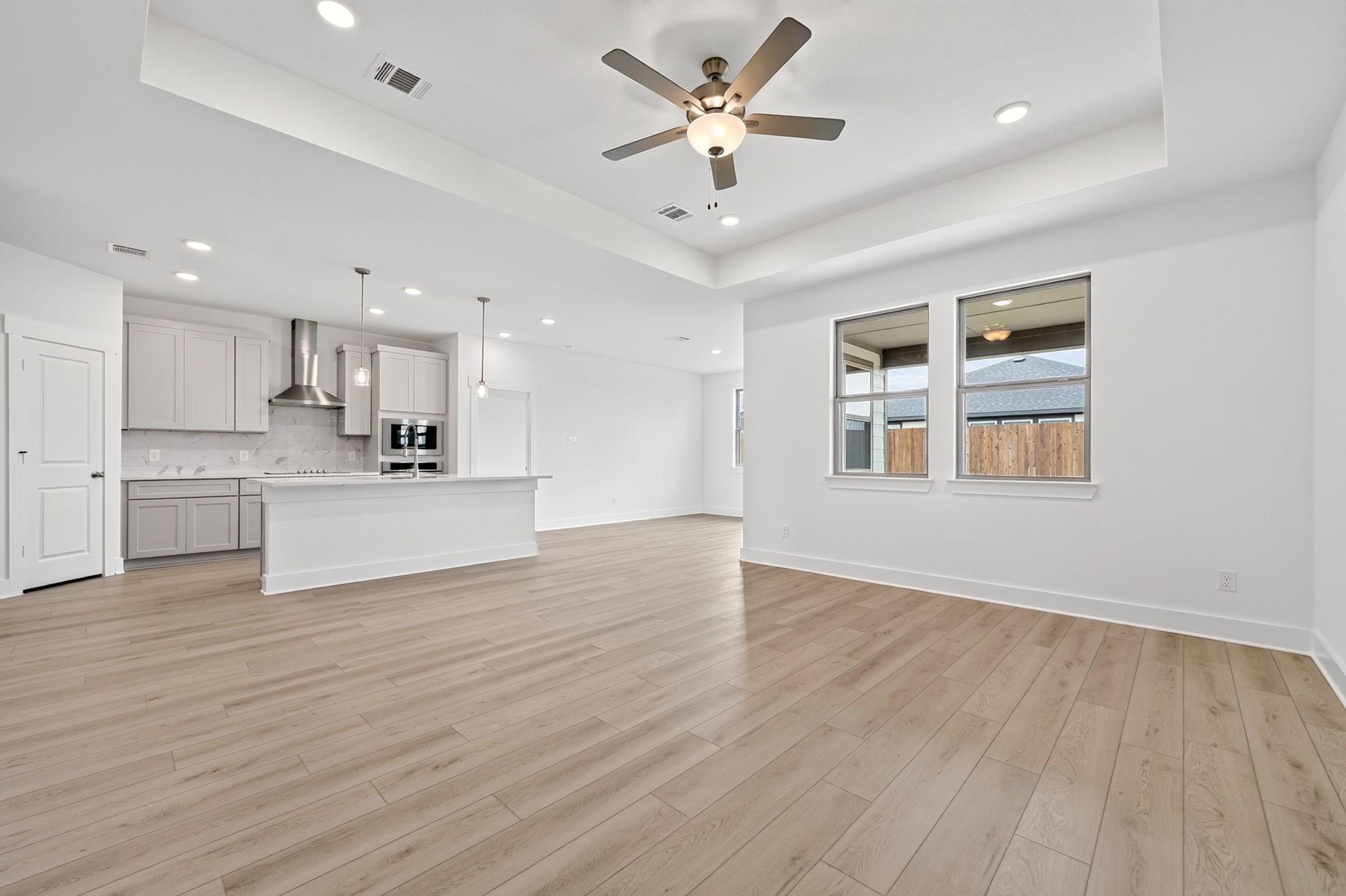 Open-concept living area with wood-look flooring, tray ceiling, and white kitchen island in Davidson Homes Holly F plan, Josephine TX