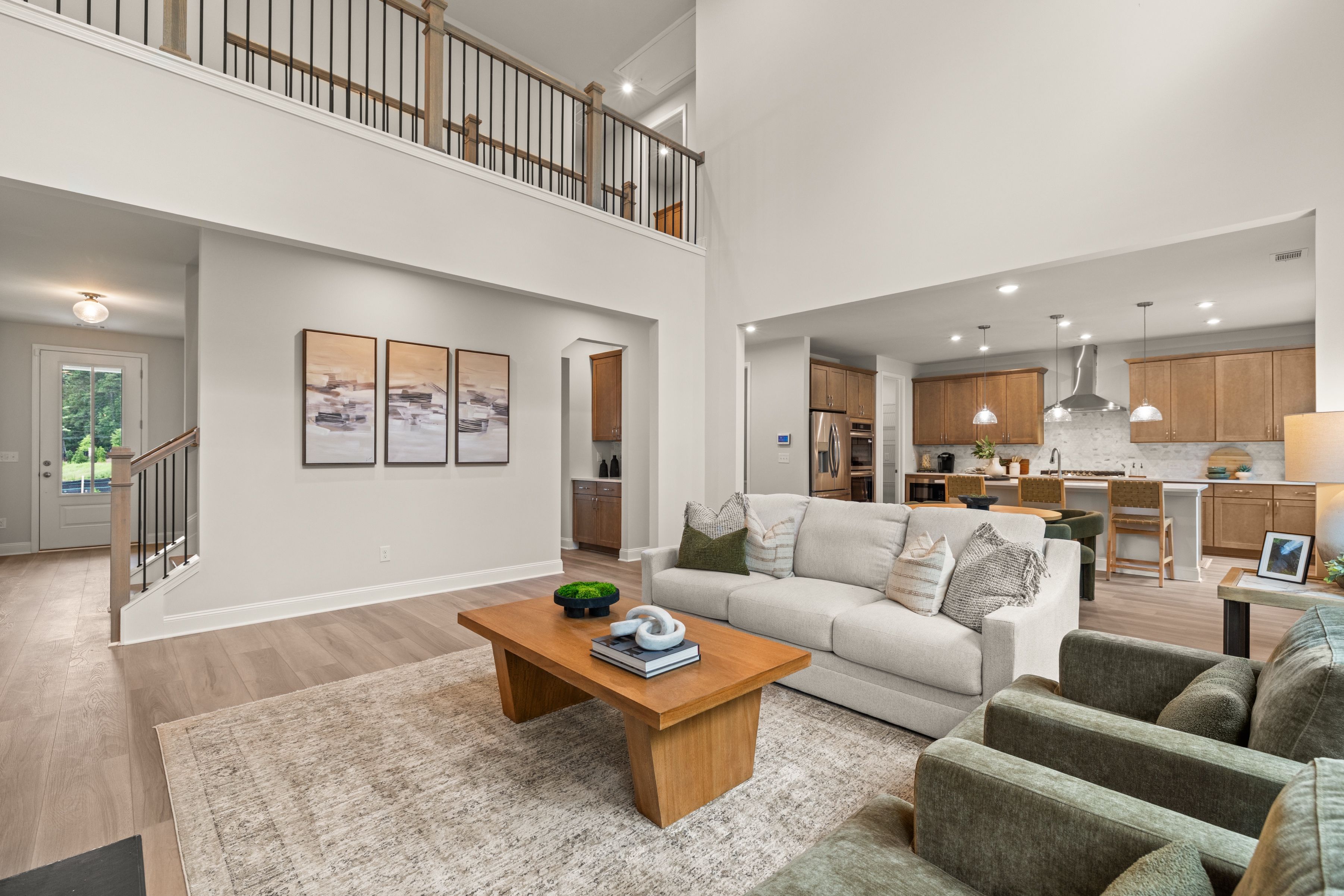 Open-concept kitchen and dining at Melody Lakeside Estates in Buford GA featuring white cabinets, island bar, round table with green chairs, hardwood floors