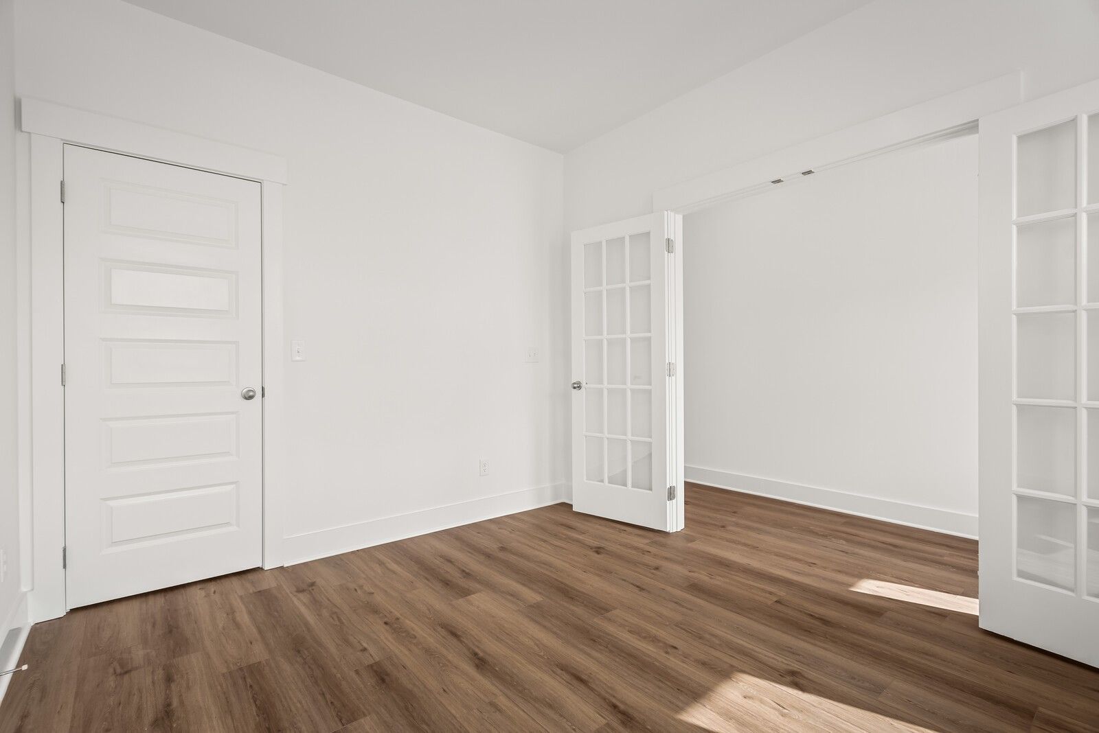 Bright empty room with white French doors, panel door, and light hardwood floors in Davidson Homes The Logan C, Gallatin, TN