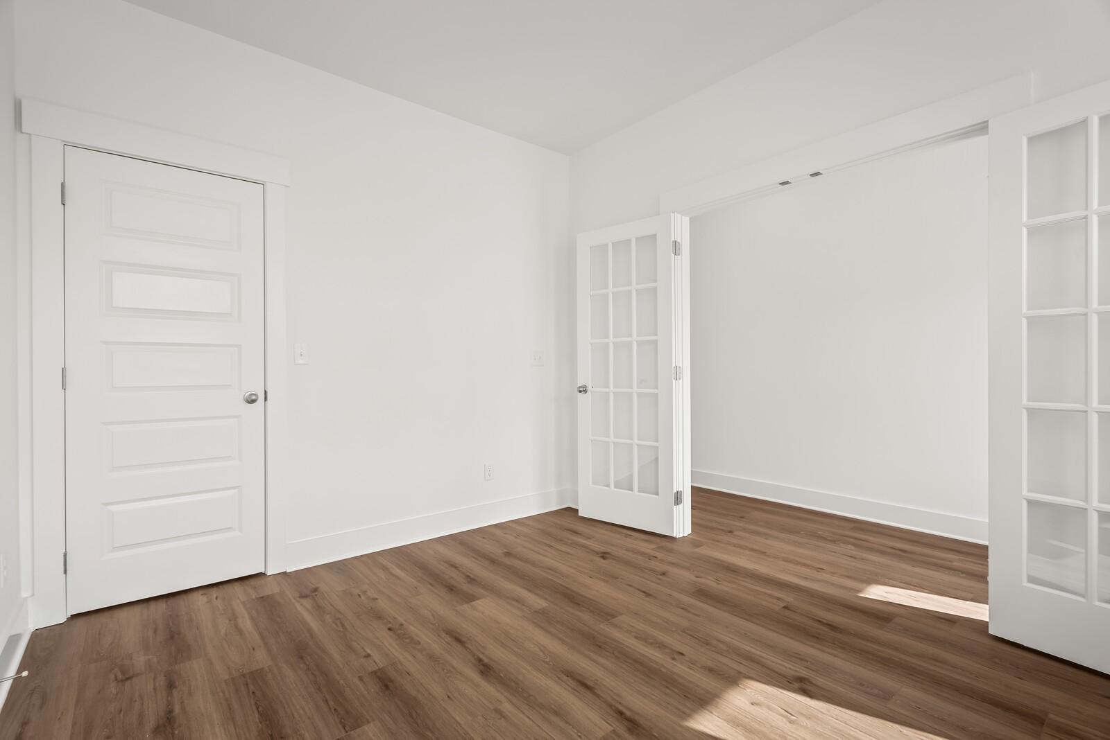 Bright empty room with white French doors, panel door, and light hardwood floors in Davidson Homes The Logan C, Gallatin, TN
