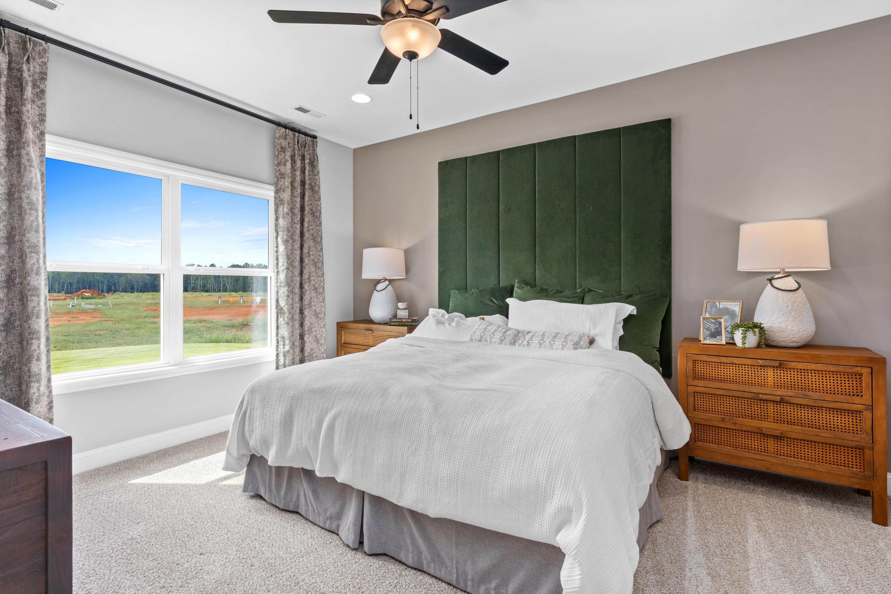 Spacious master bedroom at Wood Trail in Toney AL with green velvet headboard, king bed, and scenic field view through large window