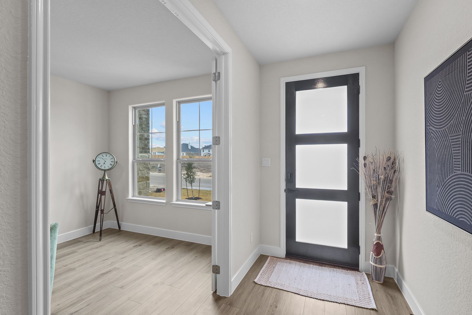 Bright entryway and home office space in The Belmont G featuring modern glass-paneled door and wood-style flooring.