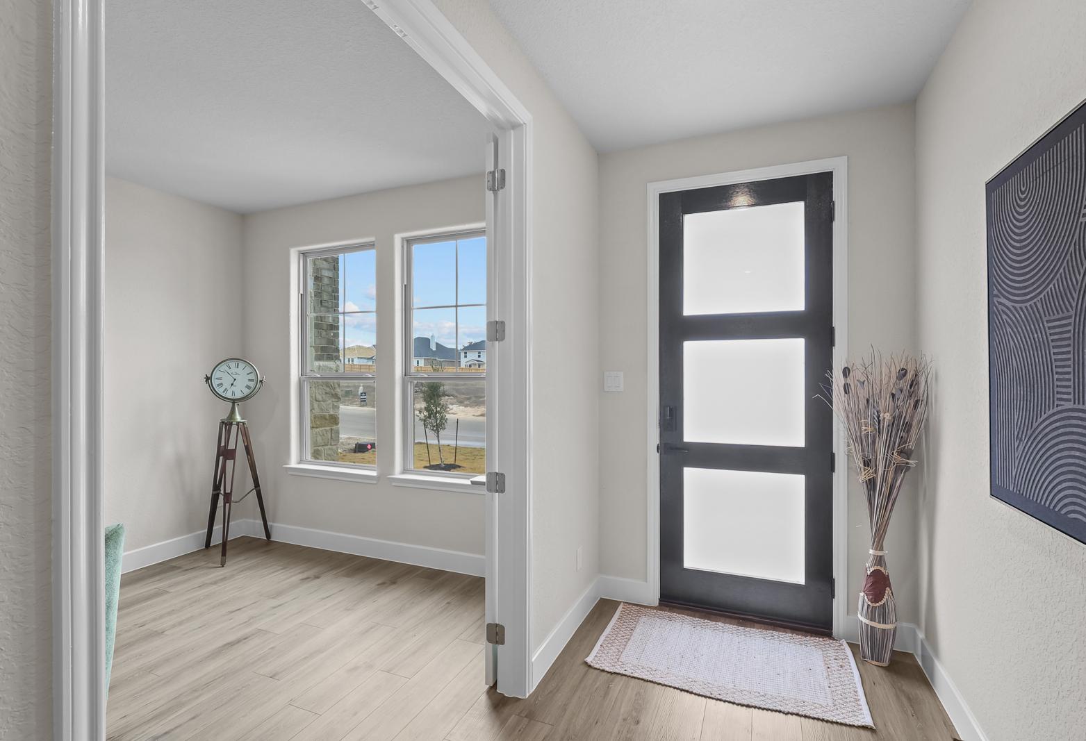 Bright entryway and home office space in The Belmont G featuring modern glass-paneled door and wood-style flooring.