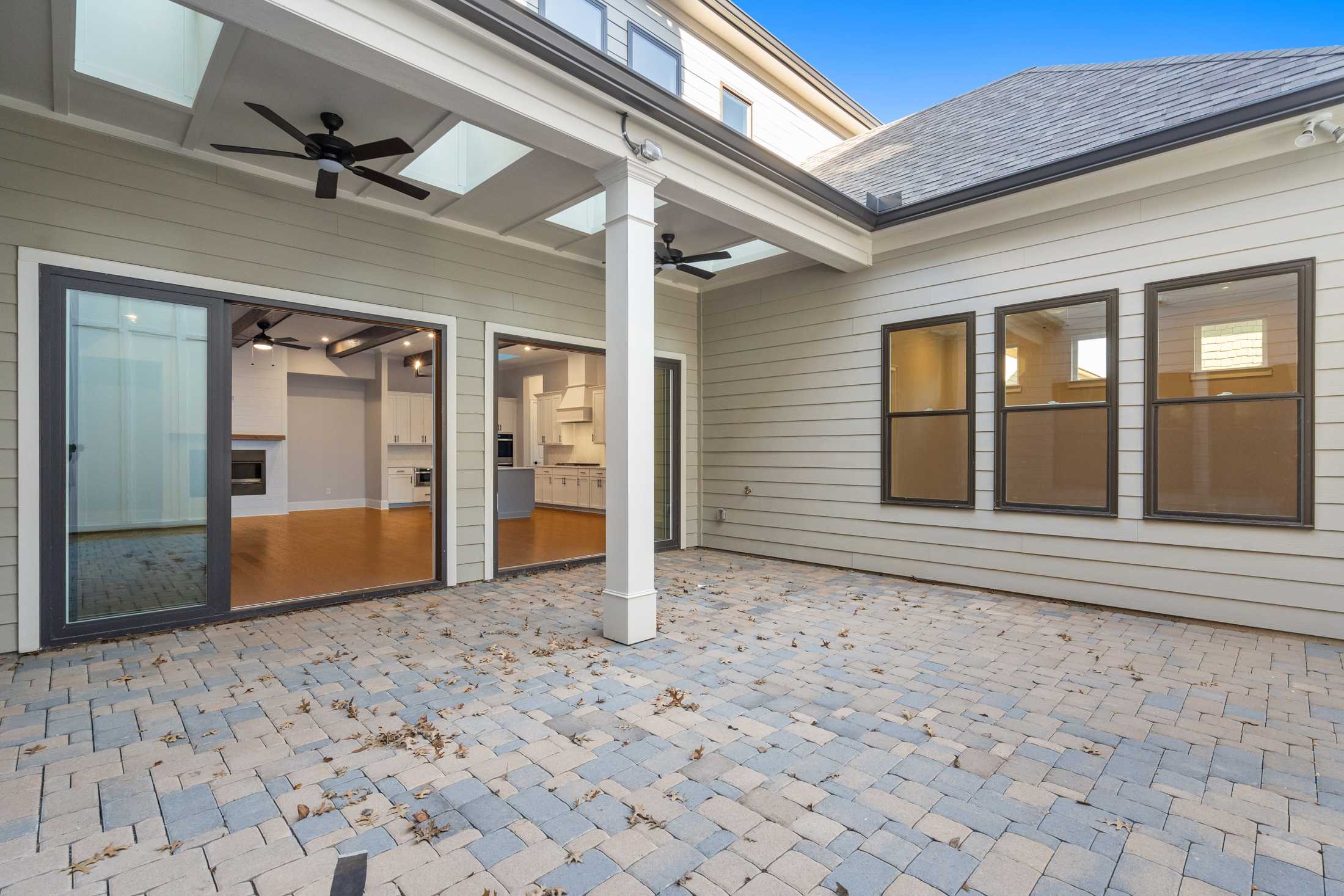 Covered patio of The Seaside home design with ceiling fans, skylights, large glass doors to paver deck and kitchen view