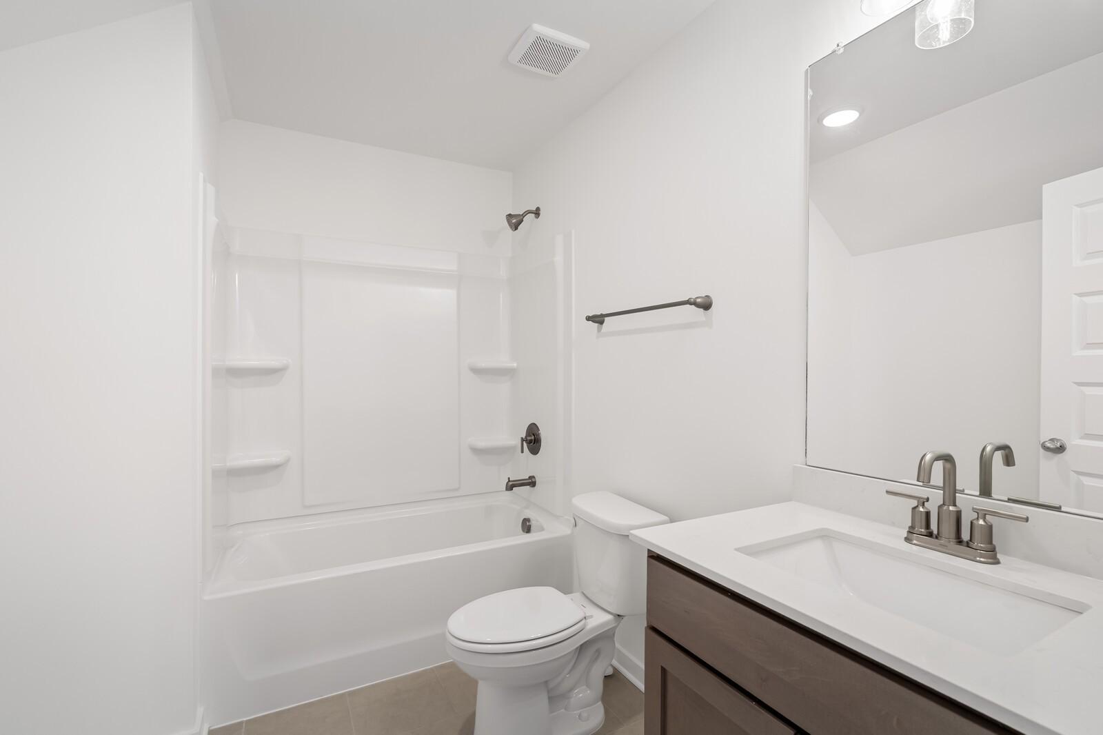 Bright white secondary bathroom with tub-shower combo, wood vanity, and mirror in Davidson Homes The Ash C, Benders Cove, Mt. Juliet, TN