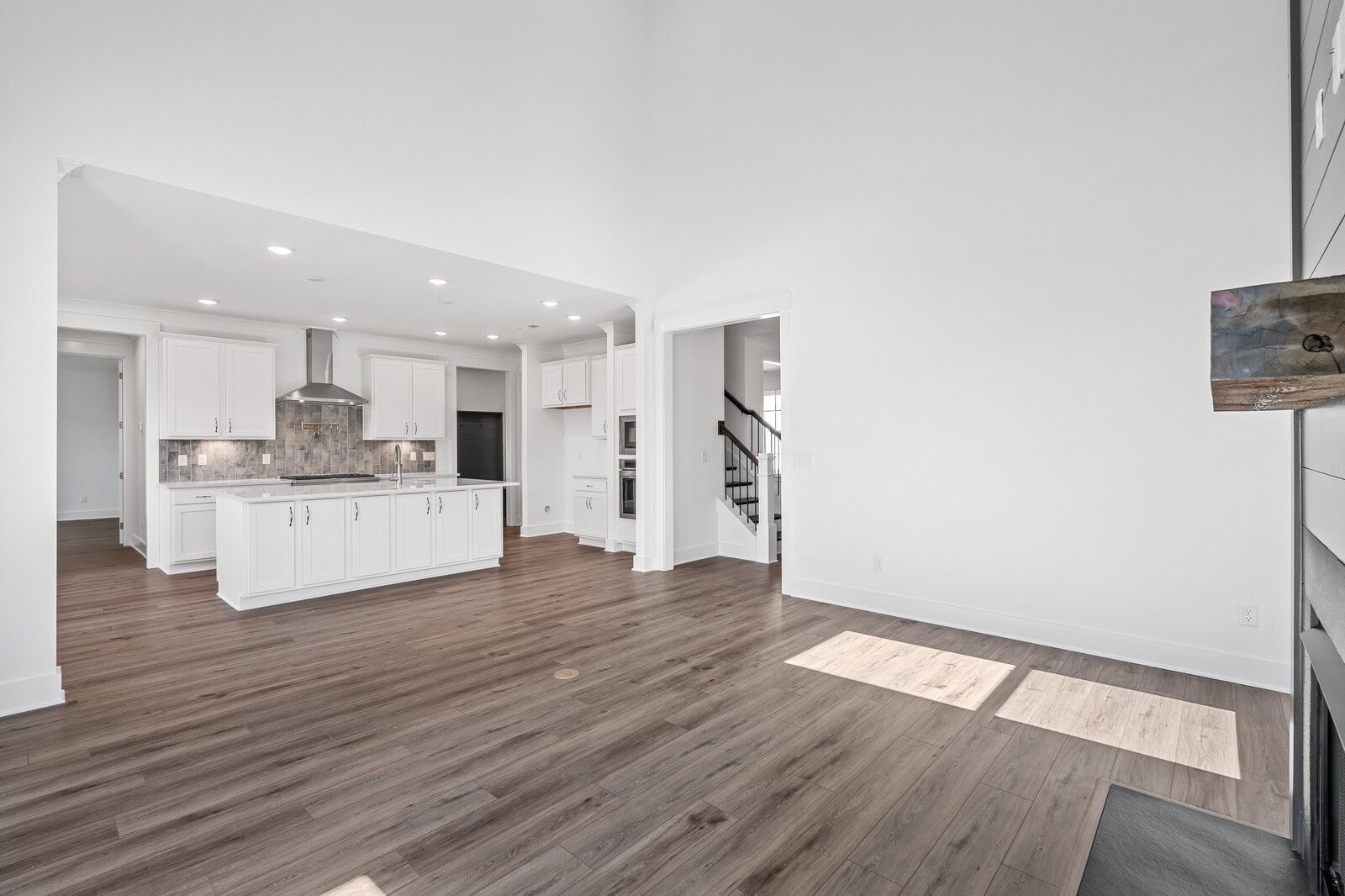Open-concept great room with stone fireplace, hardwood floors, and adjacent white kitchen island in Davidson Homes The Hawkins, Murfreesboro, TN