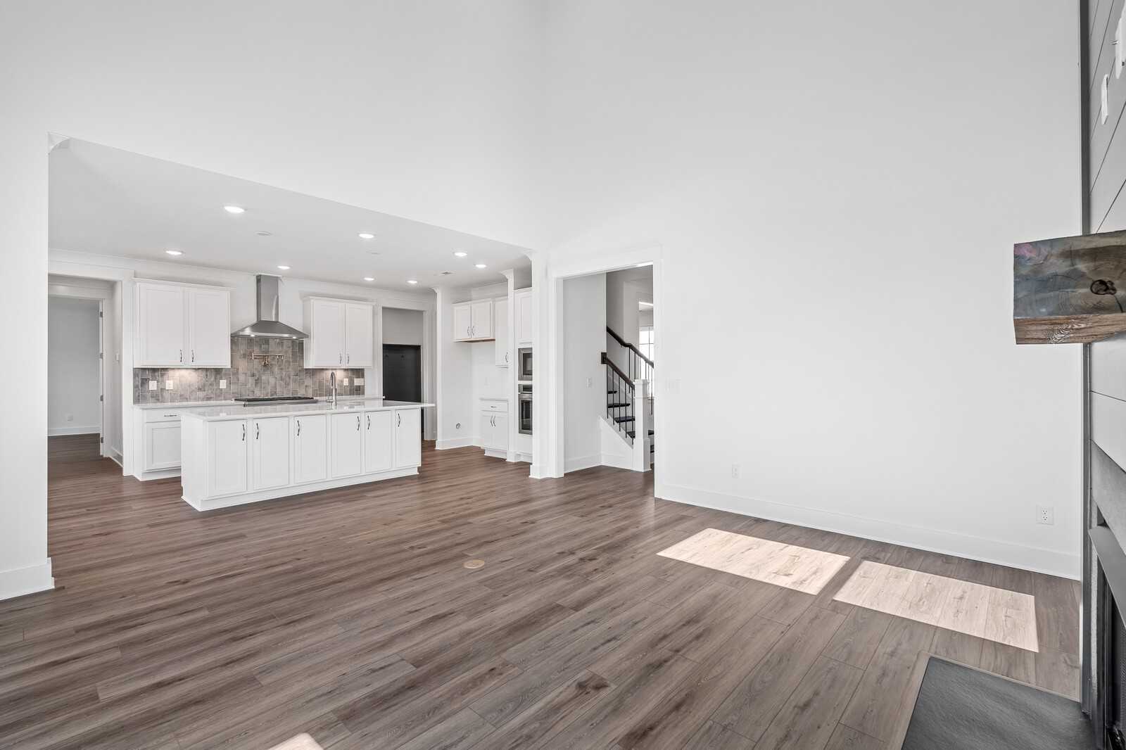 Open-concept great room with stone fireplace, hardwood floors, and adjacent white kitchen island in Davidson Homes The Hawkins, Murfreesboro, TN