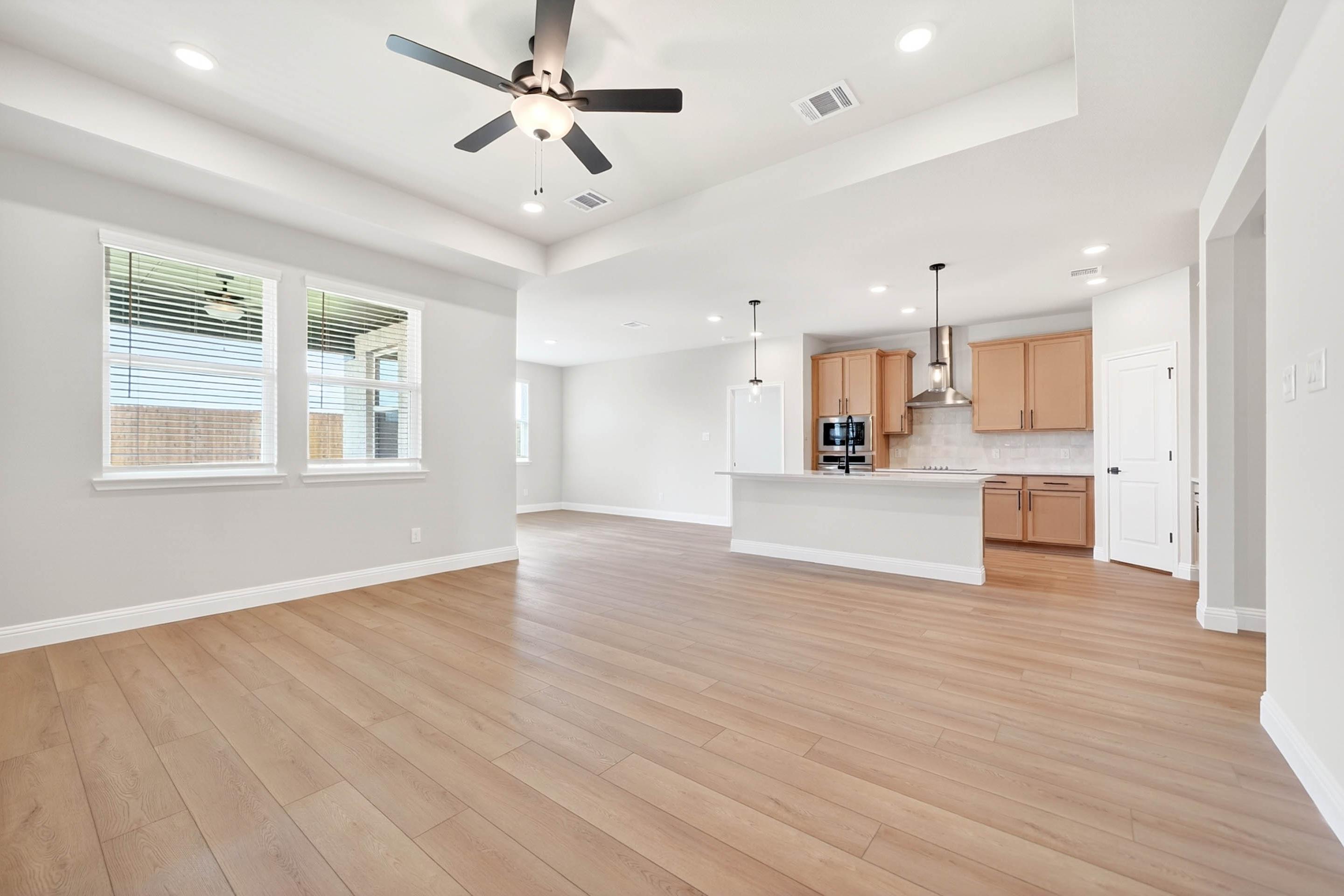 Open-concept living room and kitchen in The Holly by Davidson Homes featuring light wood flooring and modern light fixtures.