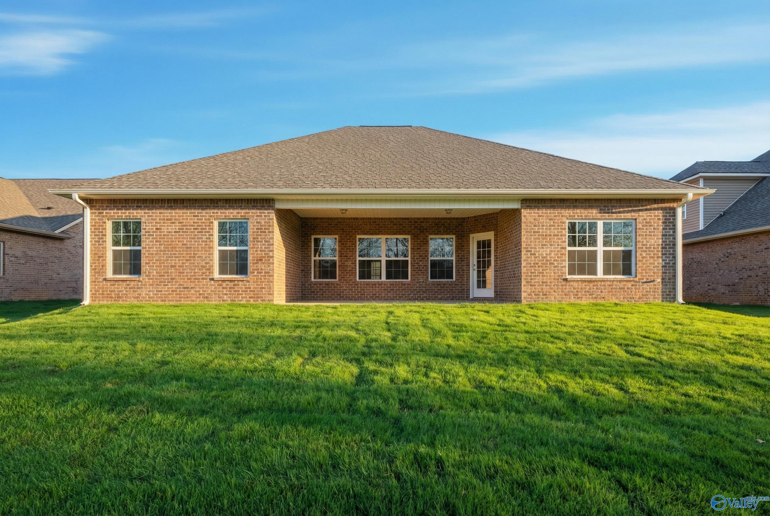 Rear view of The Rockford 3-bedroom brick home featuring covered patio and lush green lawn in Creekside, Harvest, Alabama