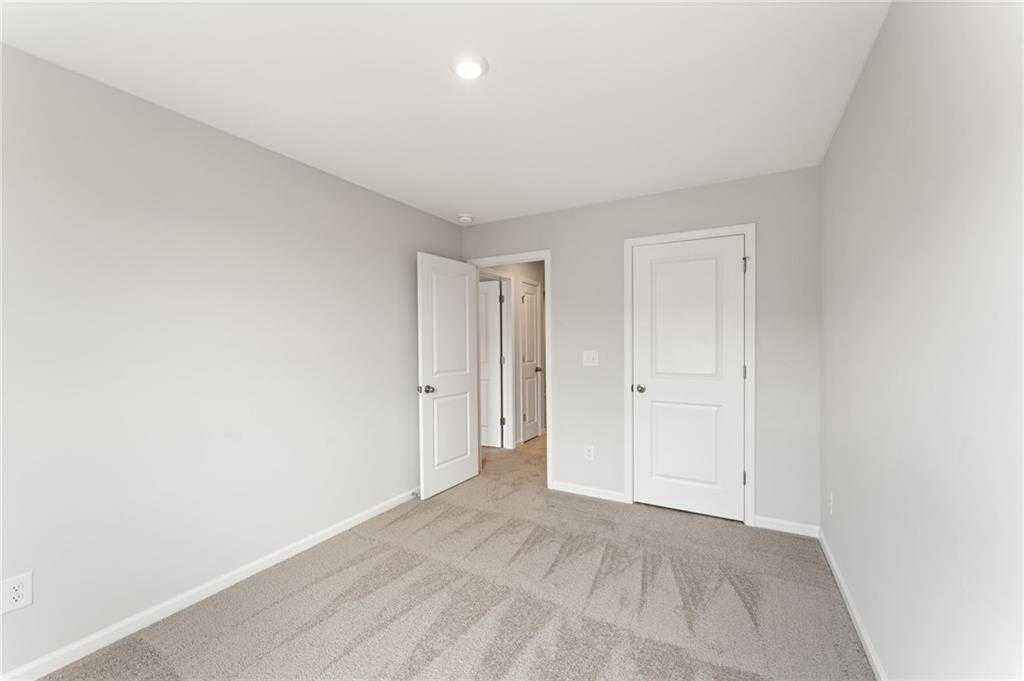 Bright secondary bedroom featuring light gray walls, white doors, and neutral carpet in Davidson Homes The Monroe A, Emerson, Georgia
